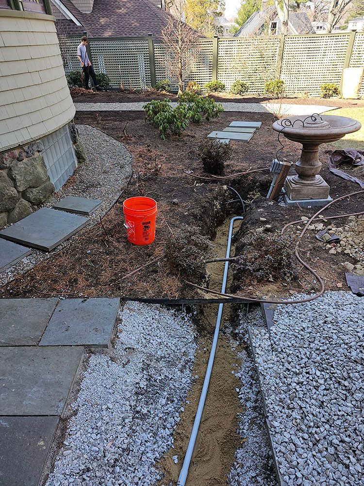 A bucket is sitting in the dirt next to a bird bath in a backyard.