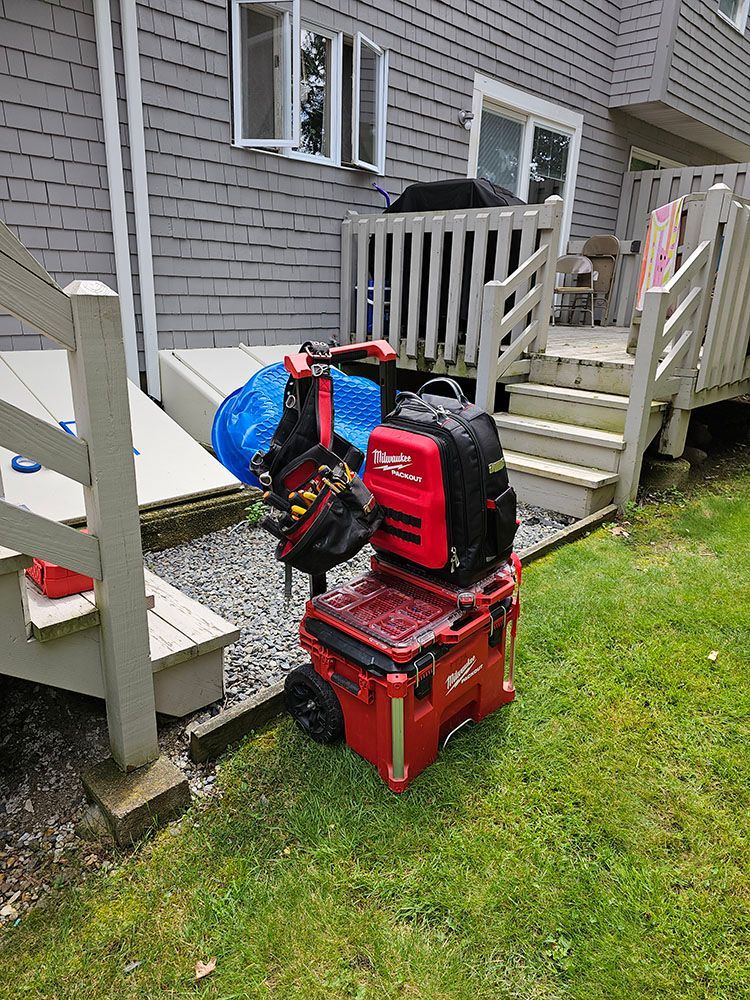 A red toolbox with a backpack on top of it is sitting on the grass in front of a house.