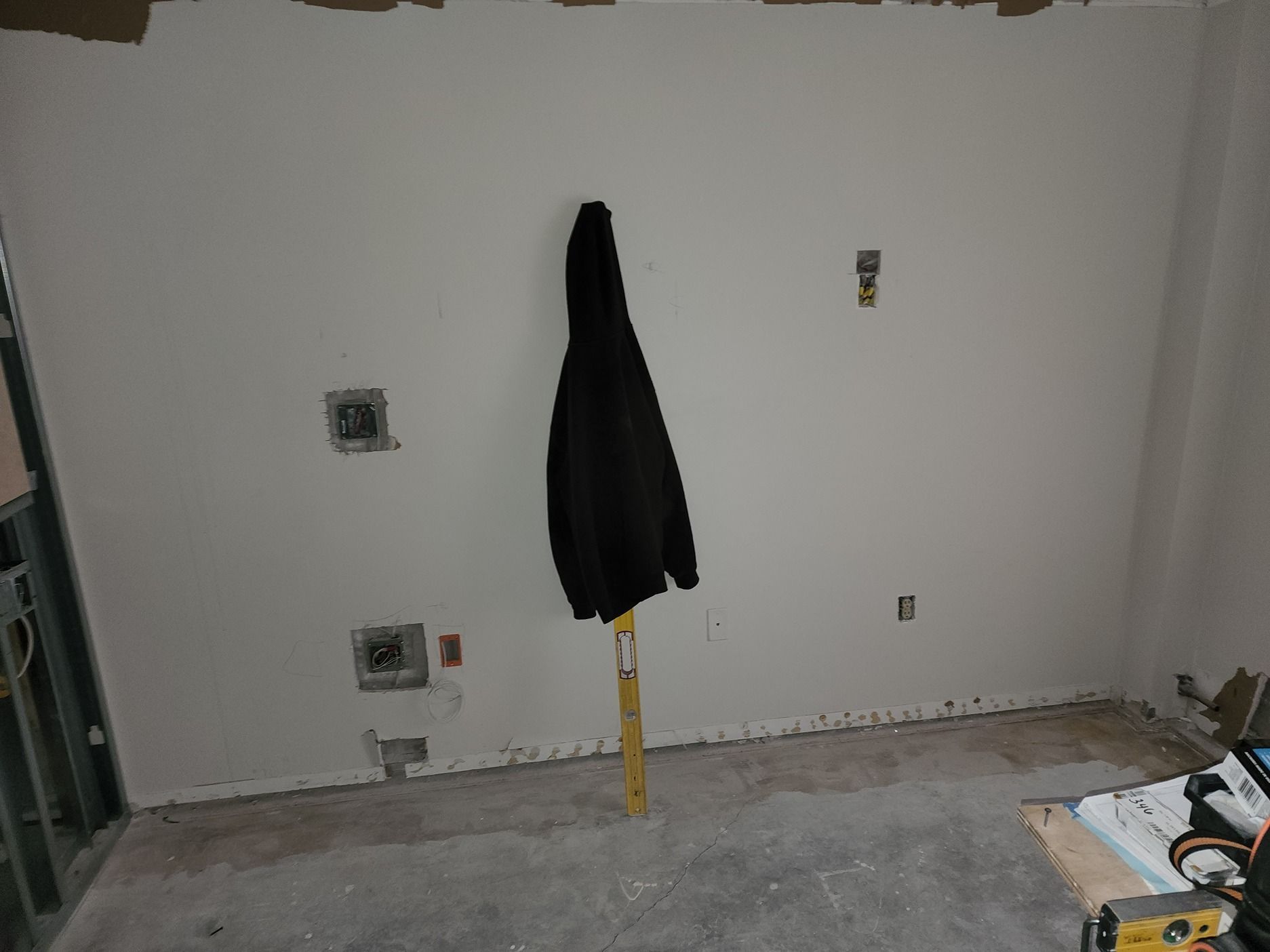 A black jacket is hanging on a yellow pole in a room under construction.