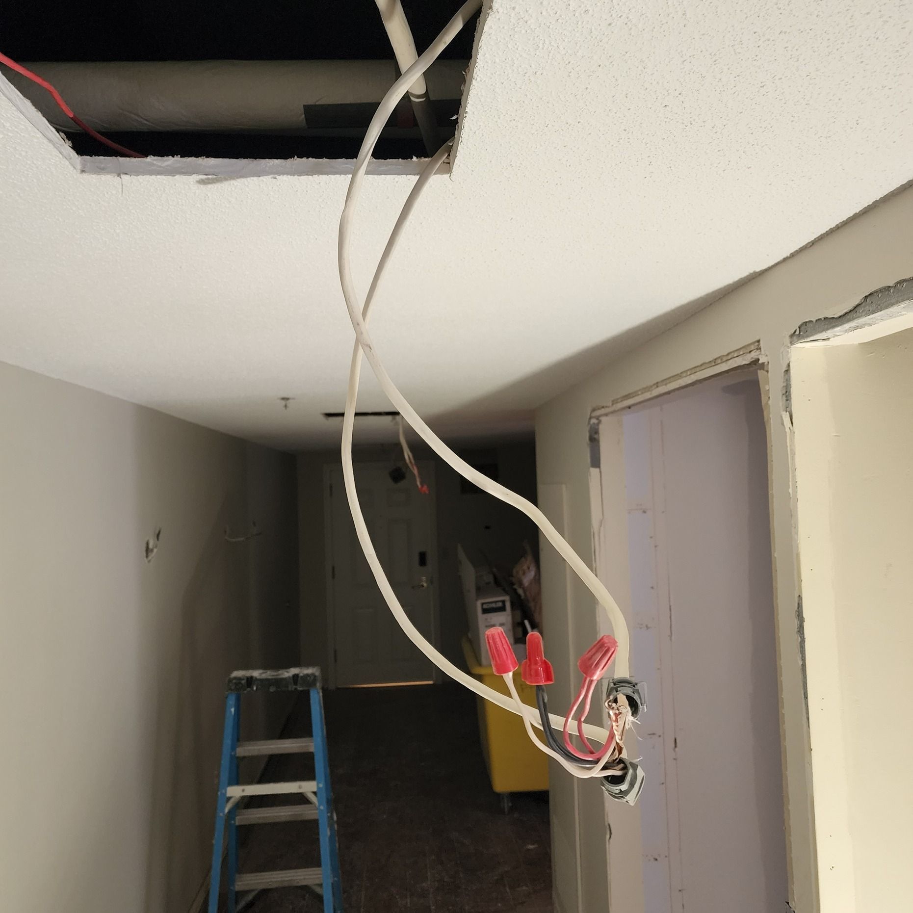 A hallway with a ladder and wires hanging from the ceiling