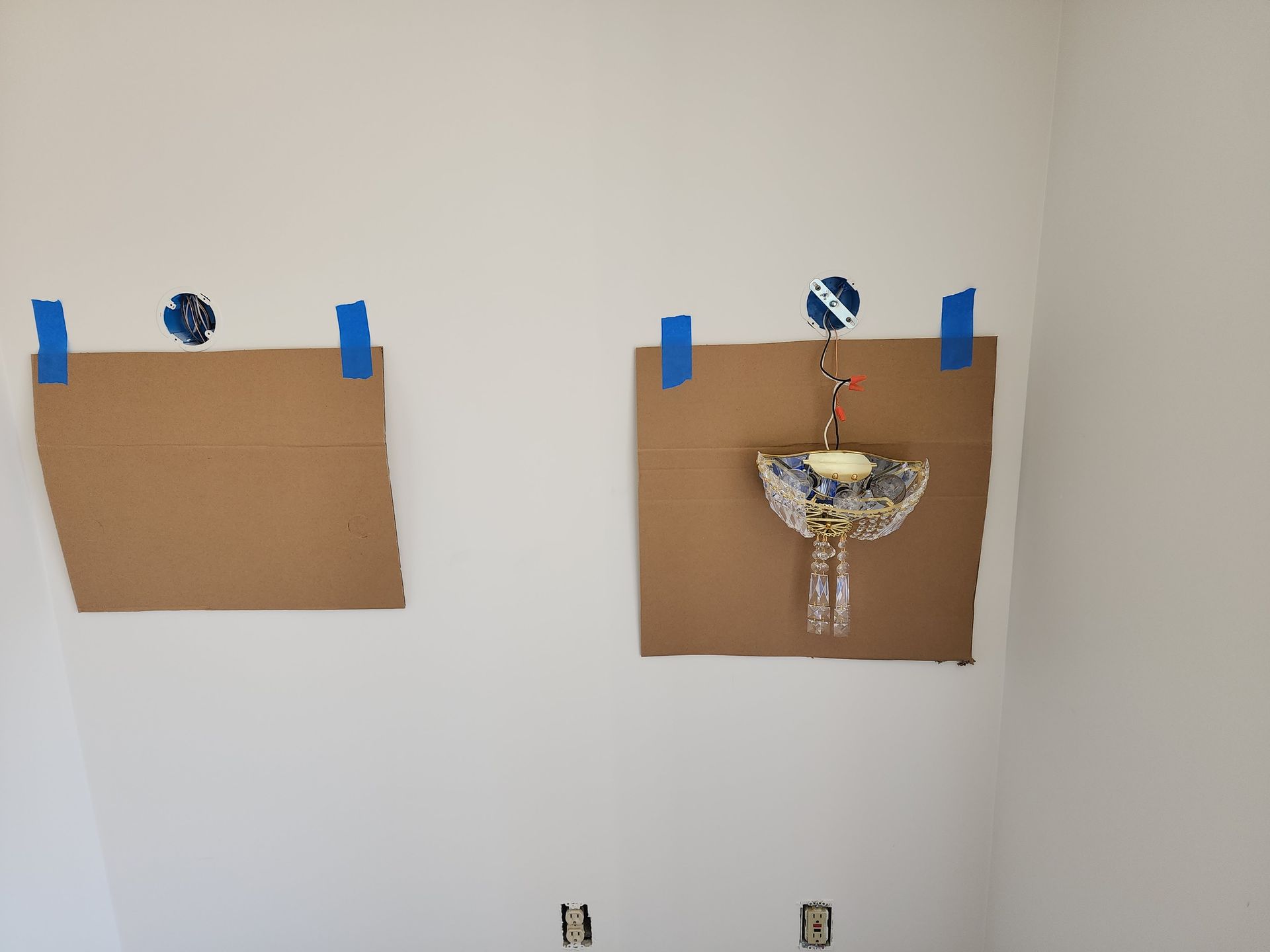 Two pieces of cardboard are taped to a wall with blue tape.