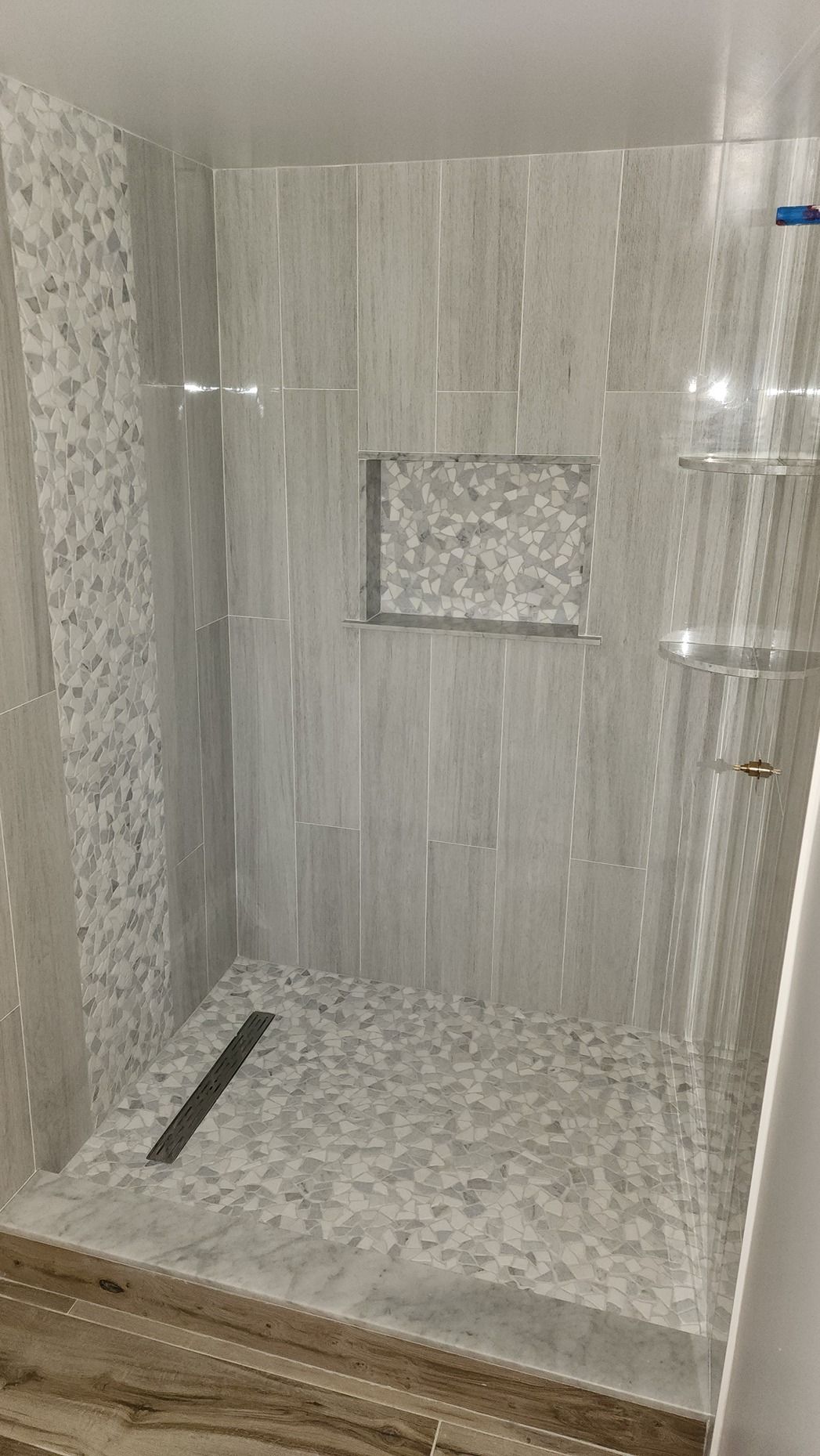 A walk in shower with a glass door and a drain.