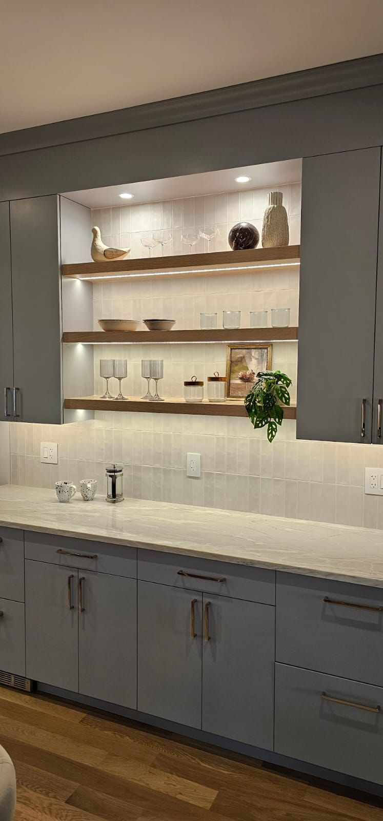 A kitchen with blue cabinets , white counter tops , and wooden shelves