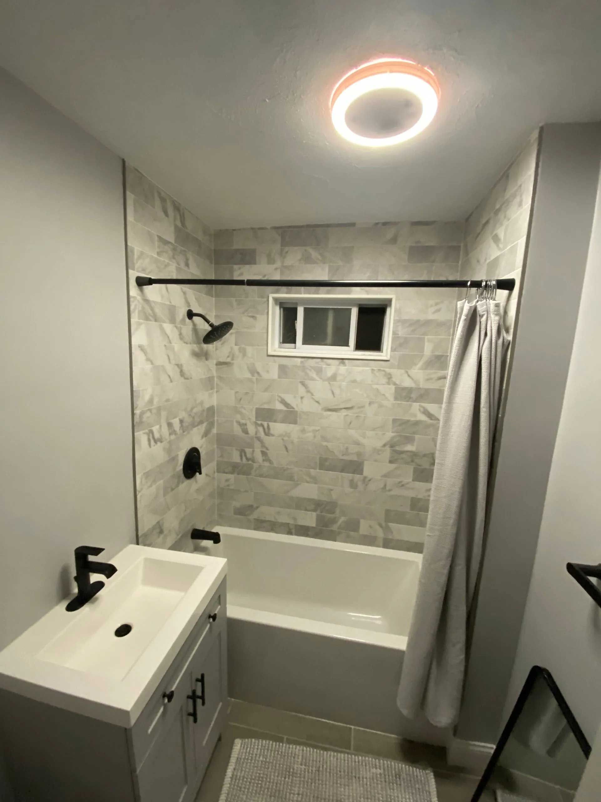 A modern bathroom with gray walls, a tiled shower, black fixtures, and a white vanity.