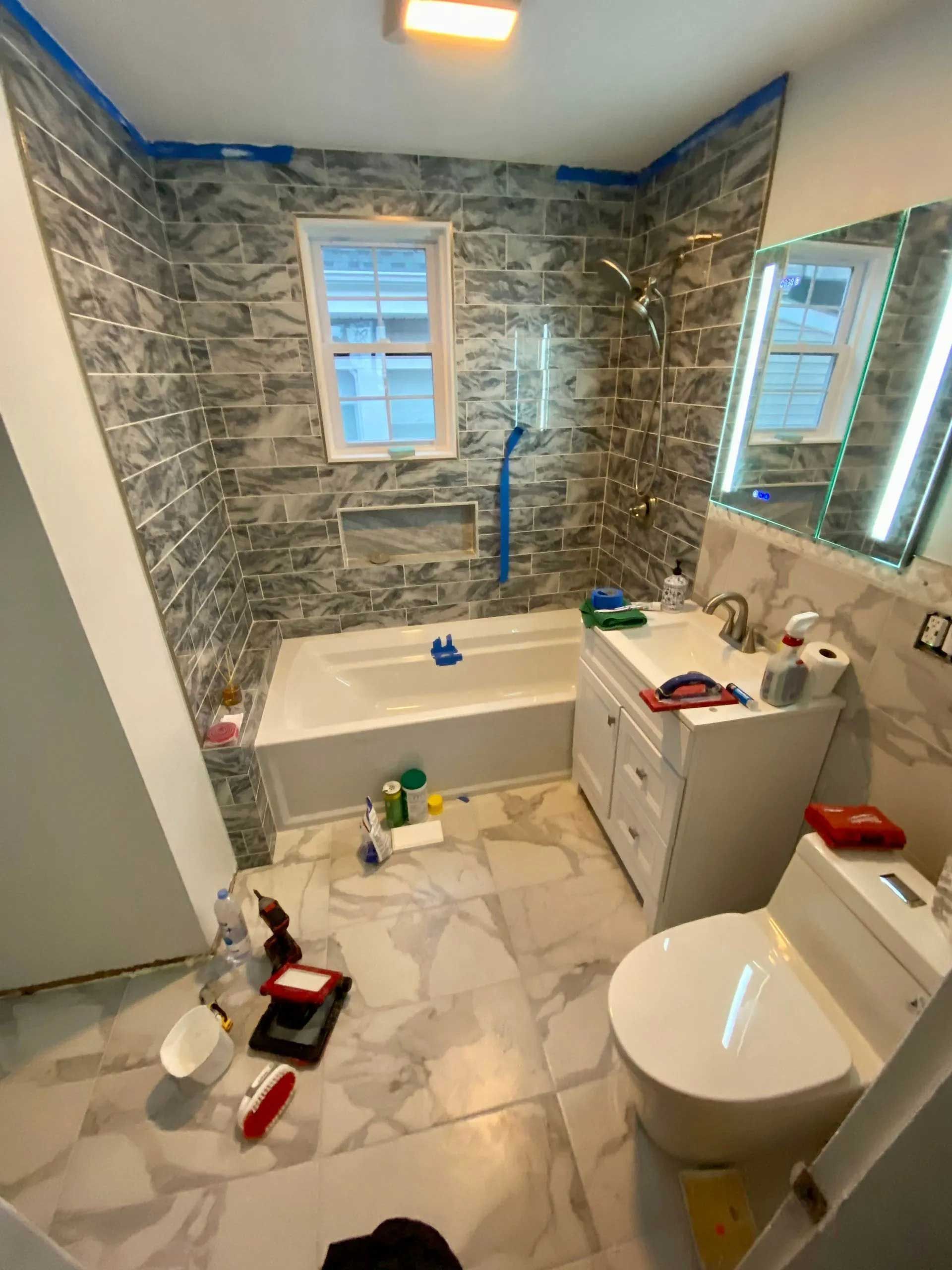 Bathroom renovation with tiled walls and floor, white fixtures, and construction tools.