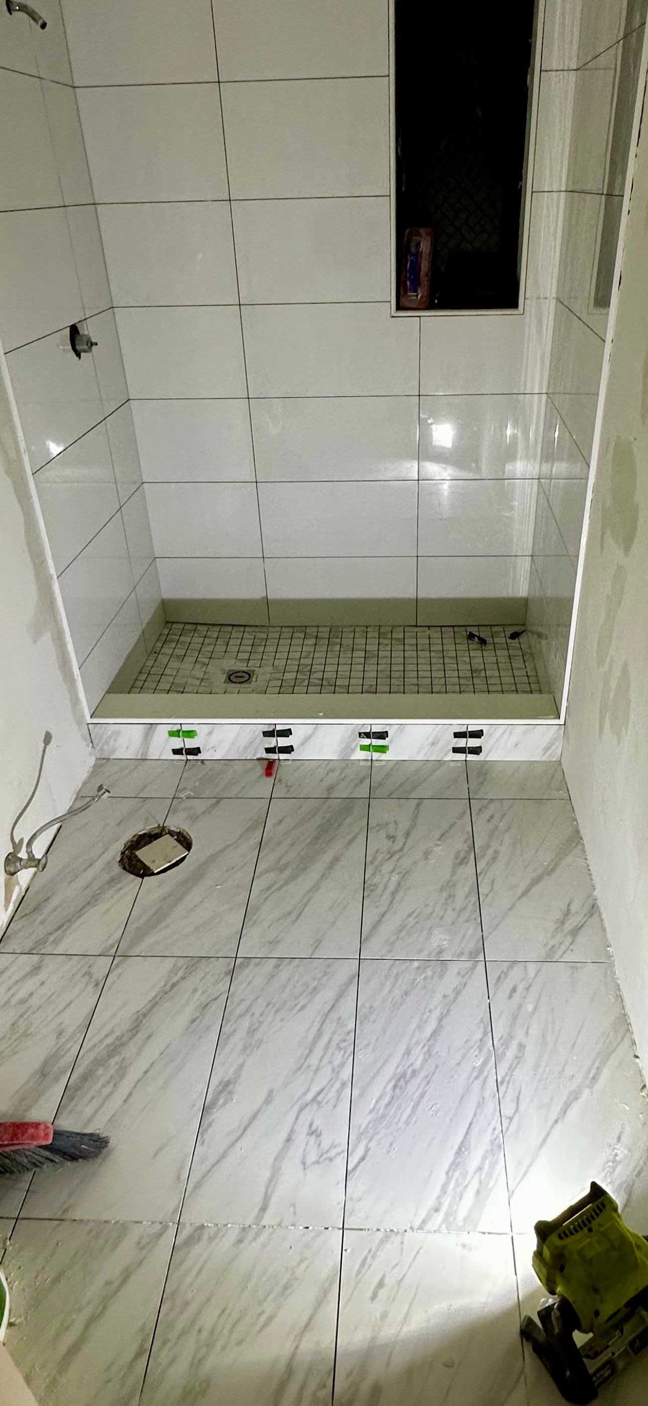A bathroom in progress. Tiled walls and floor with shower basin visible.