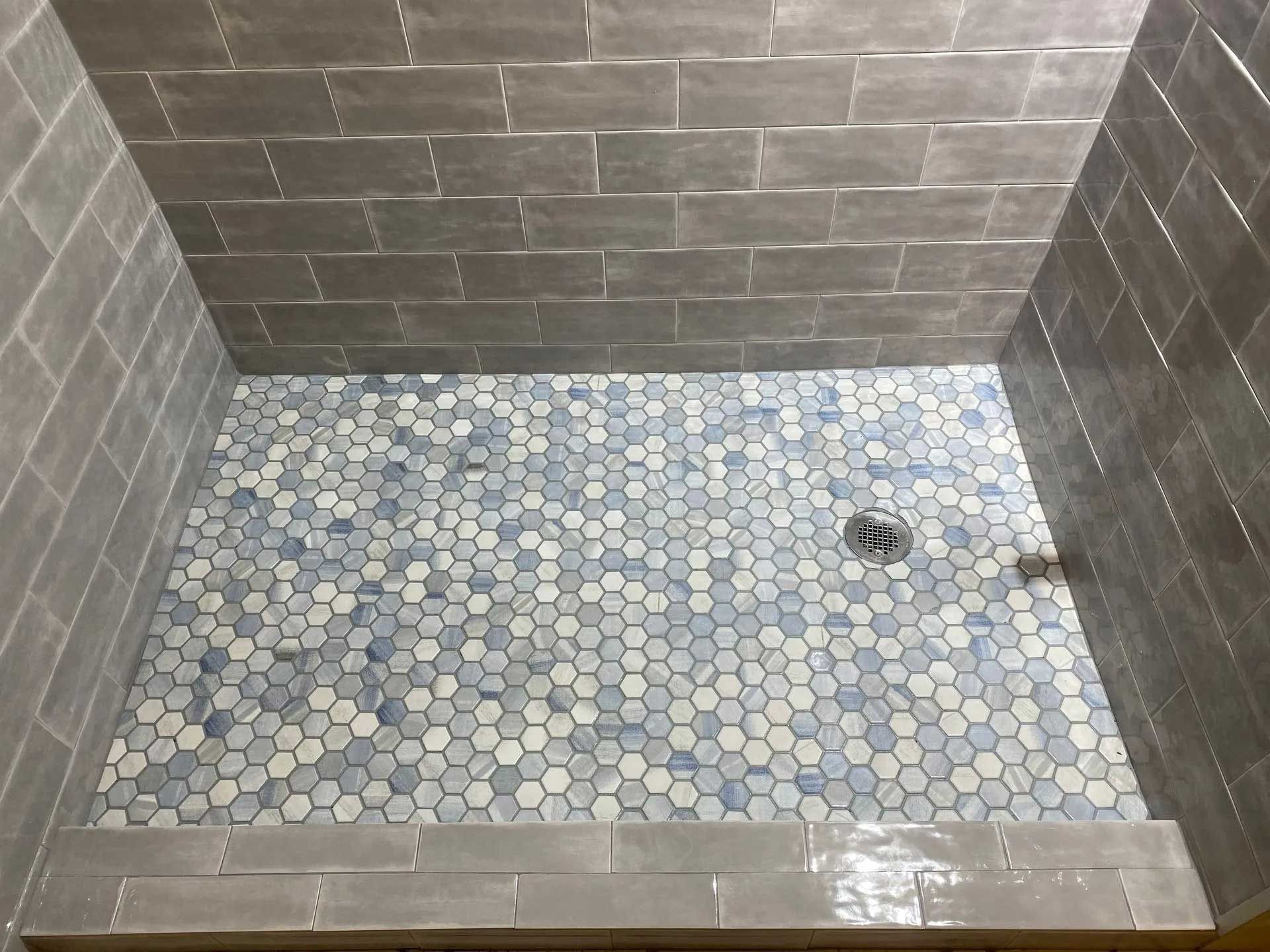 Gray tiled shower with a mosaic hexagon tile floor, drain visible.