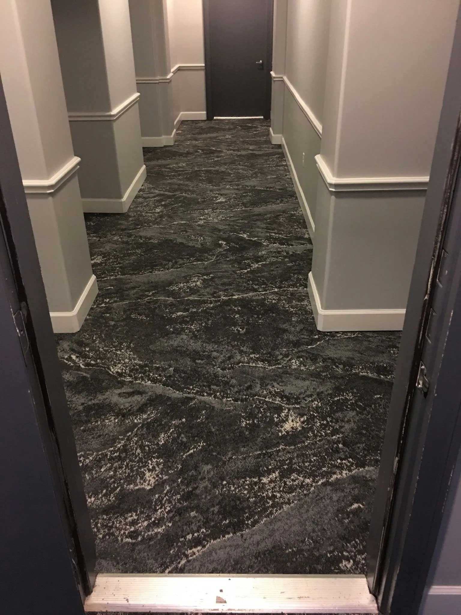 Hallway with patterned carpet, gray pillars, and a dark door at the end.