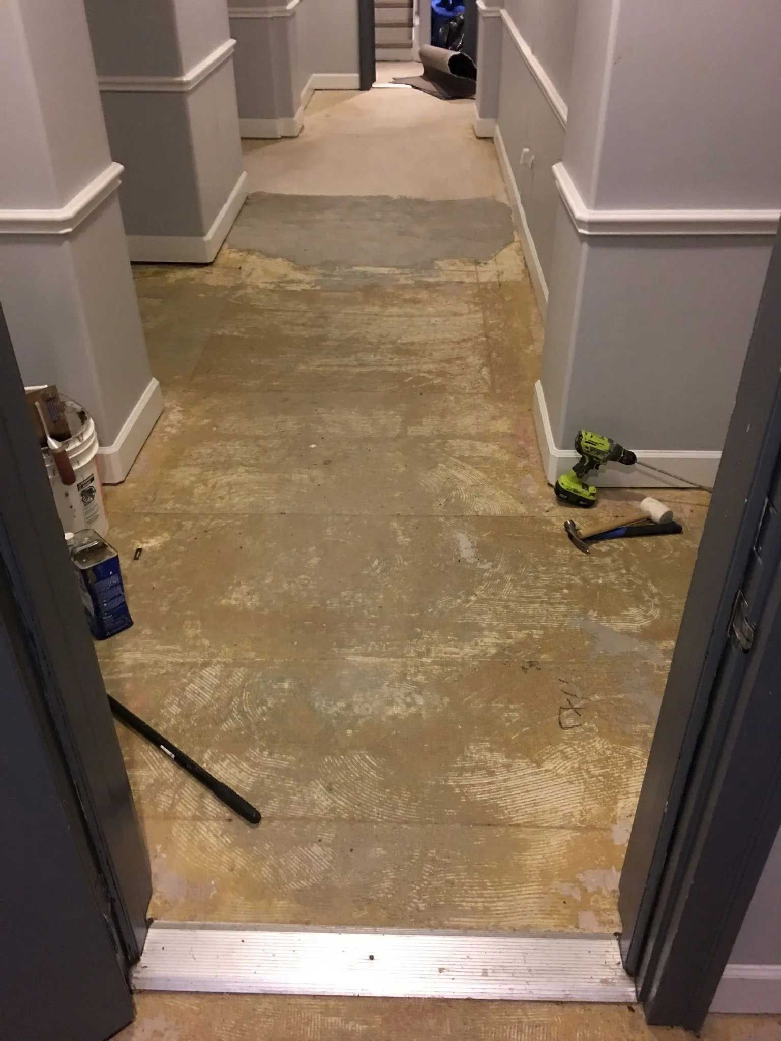 Hallway with exposed subfloor. Gray walls, white trim, tools, and debris are visible.