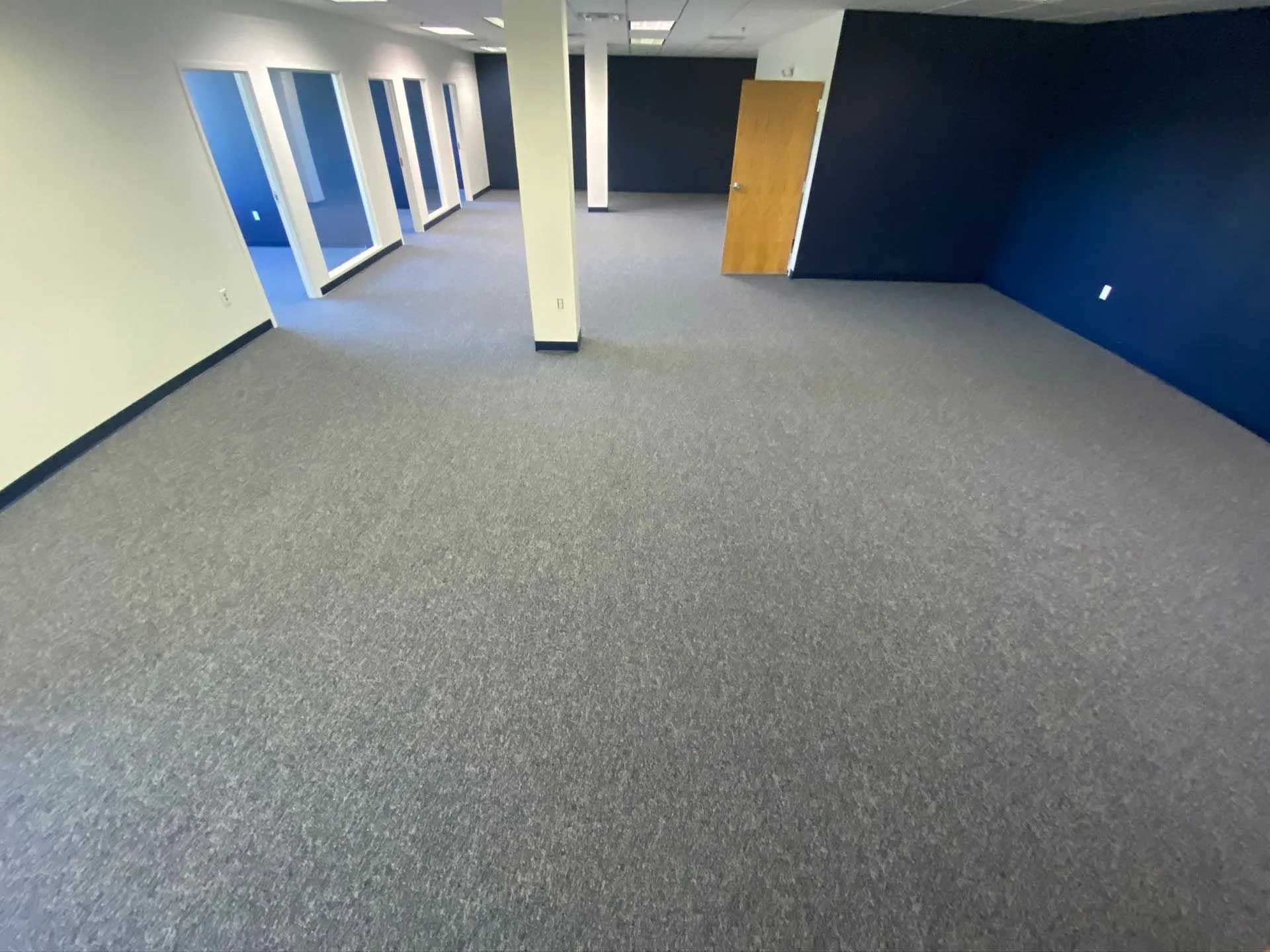 Empty office space with blue and white walls, grey carpet, and a central support column.