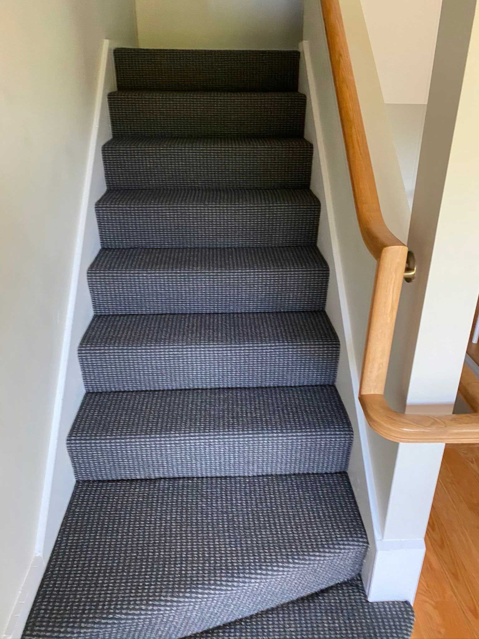 Staircase with gray patterned carpet, white risers, and wooden handrail.