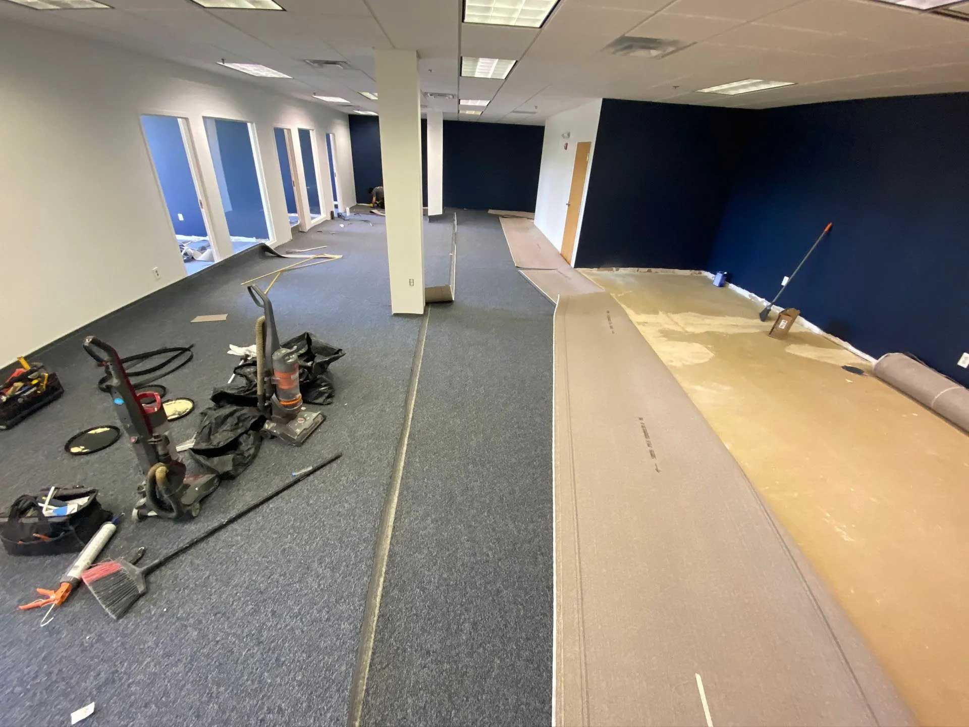 Office space undergoing renovation; new carpet being installed. Blue and beige tones, tools present.
