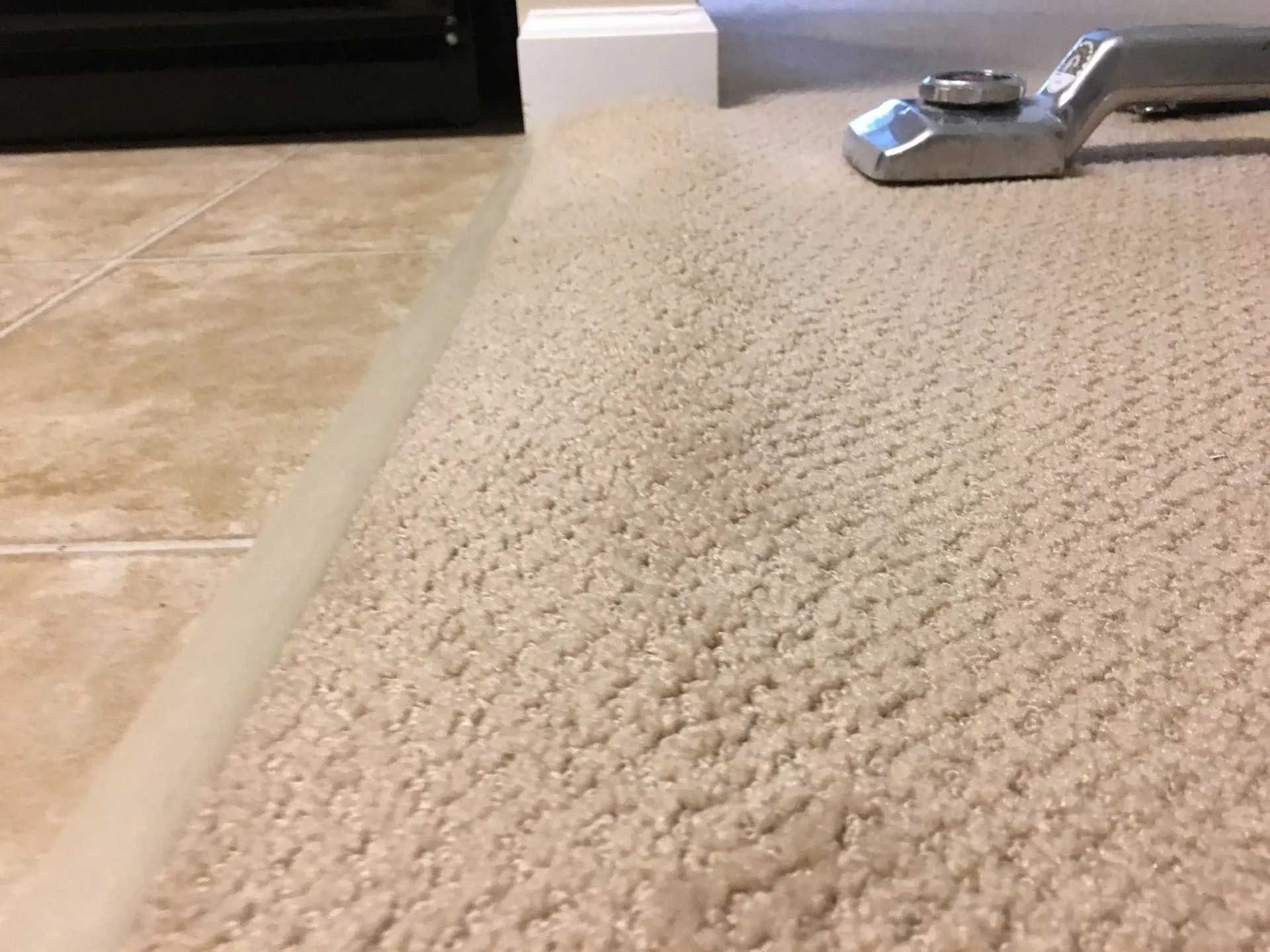 Carpet being installed, with a tool securing it to the floor near a tile edge.