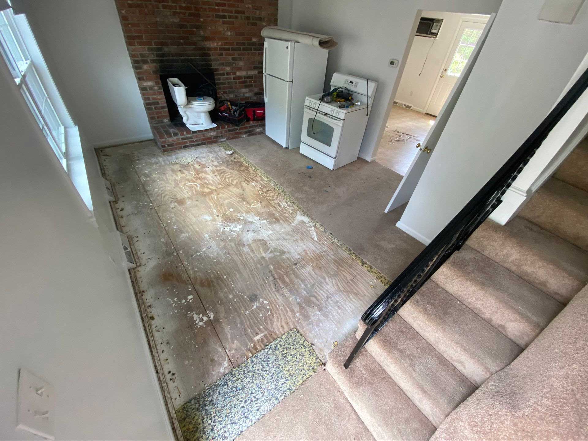 View of a room under renovation. Exposed wood floor, appliances, and stairs visible.