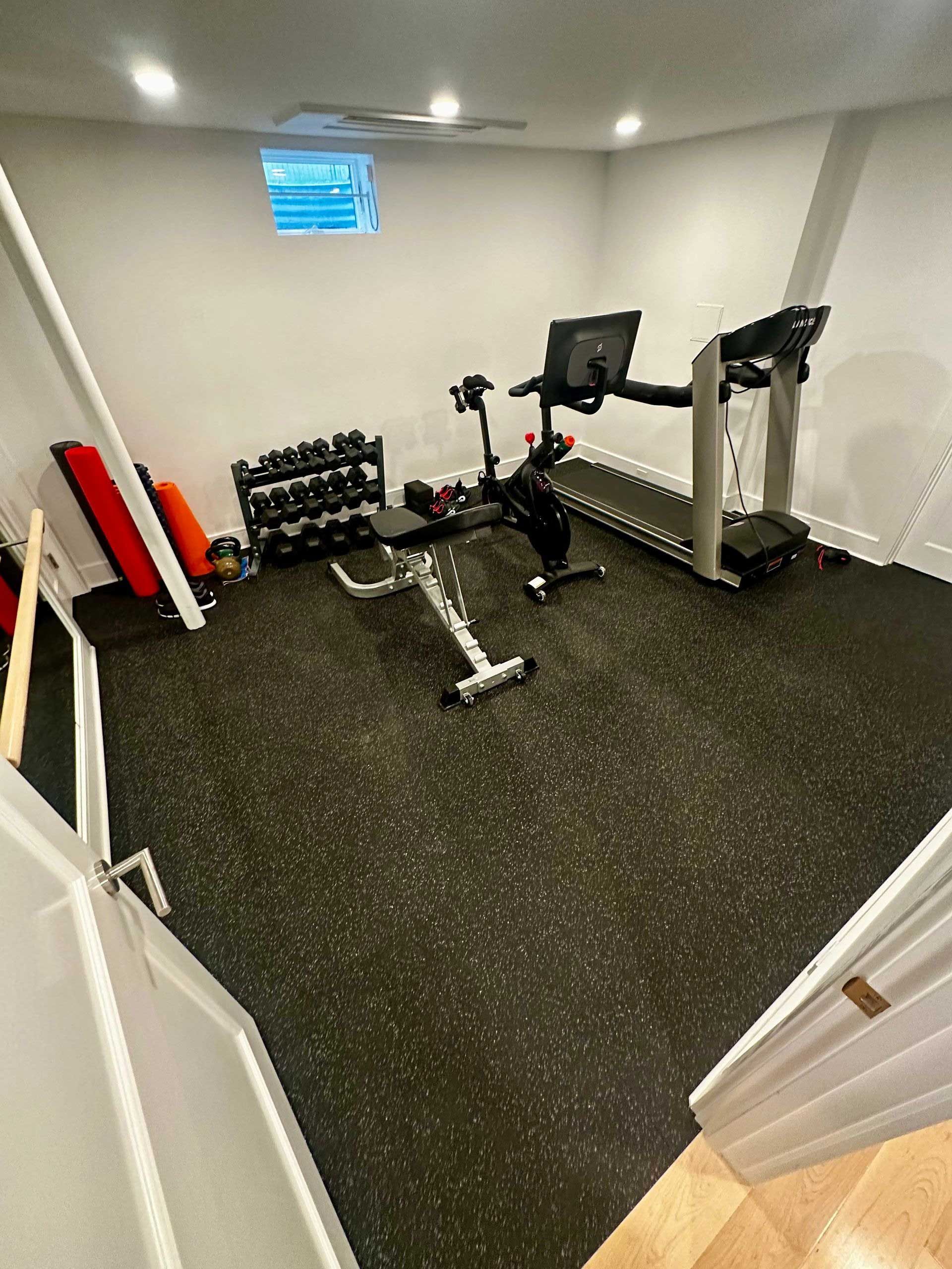 Home gym with black rubber flooring, treadmill, weights, and exercise bike.
