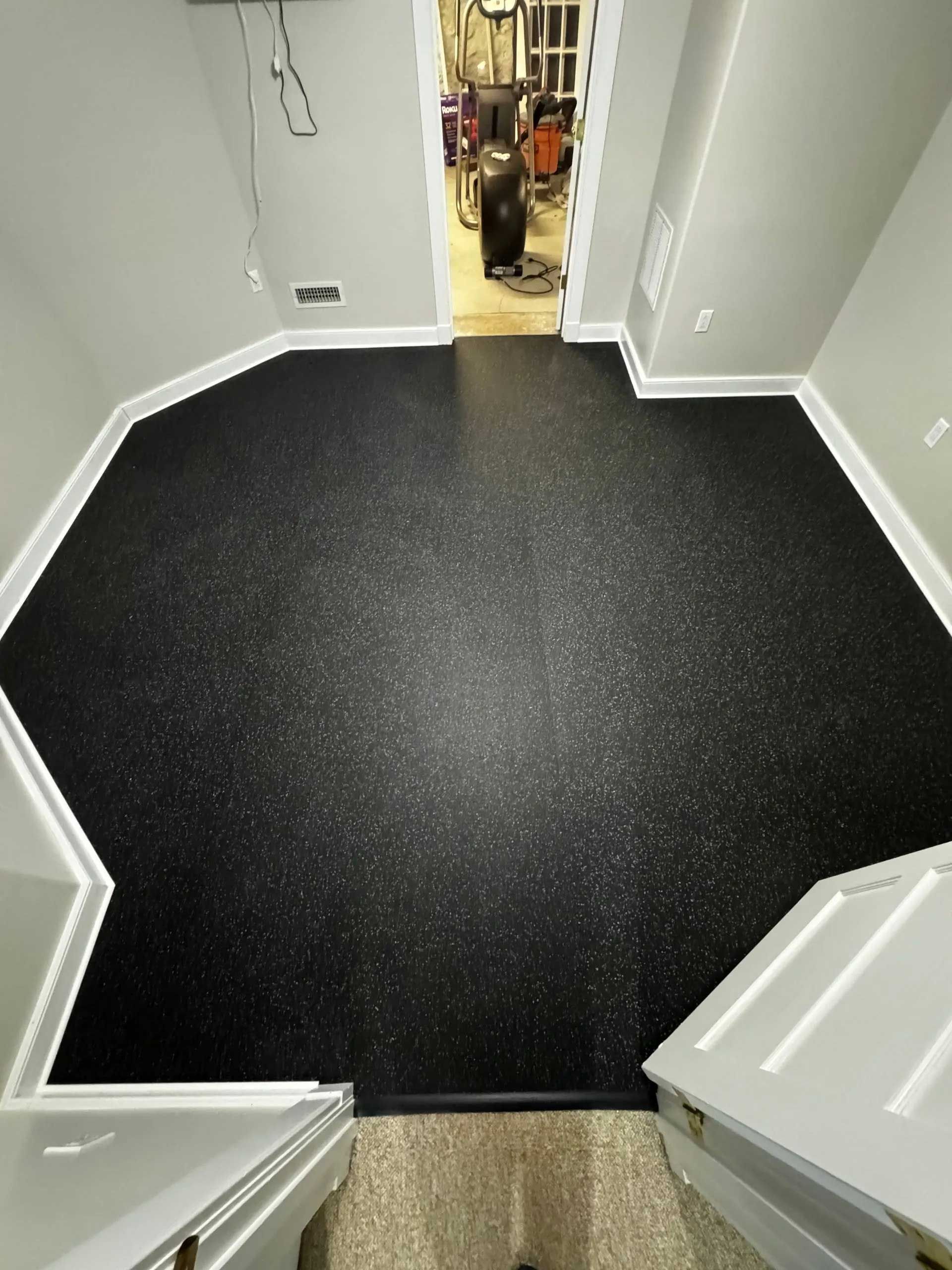 Black speckled flooring in room with white trim and doorways.
