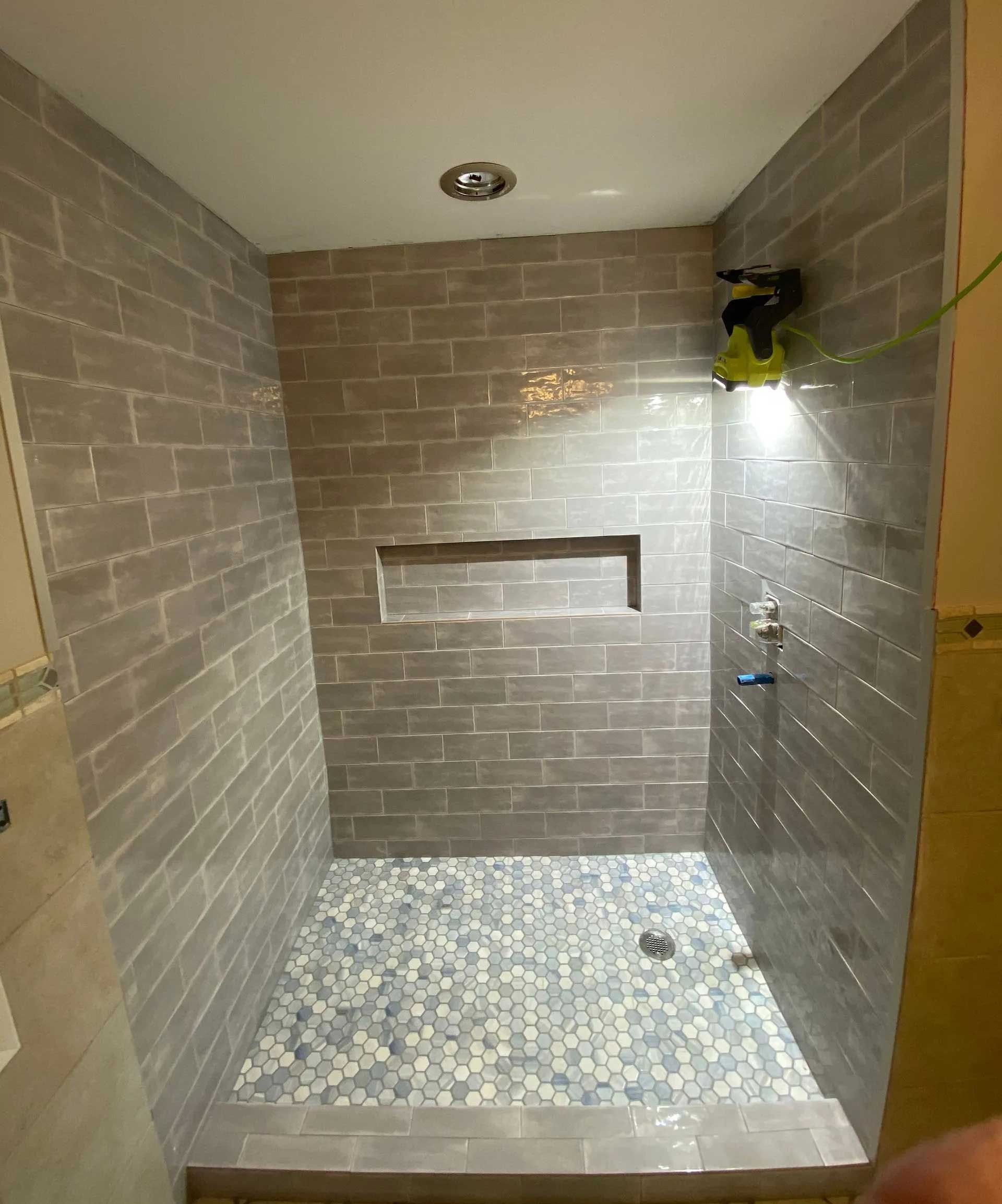 Shower stall with gray tiled walls, pebble floor, and a recessed shelf.