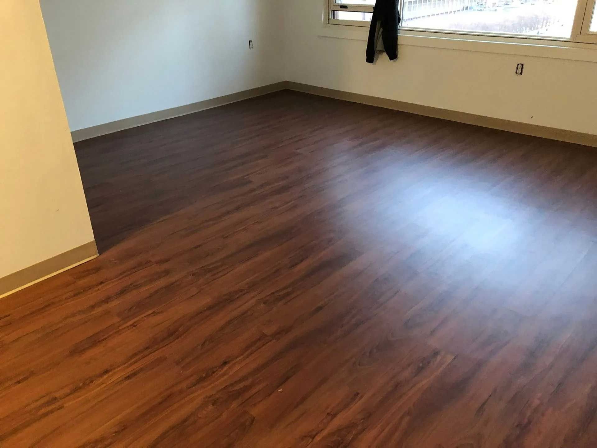 Empty room with brown wood-look laminate flooring and a window.