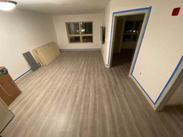 Empty room with wood-look flooring, white walls, and blue painter's tape around a doorway and baseboards.