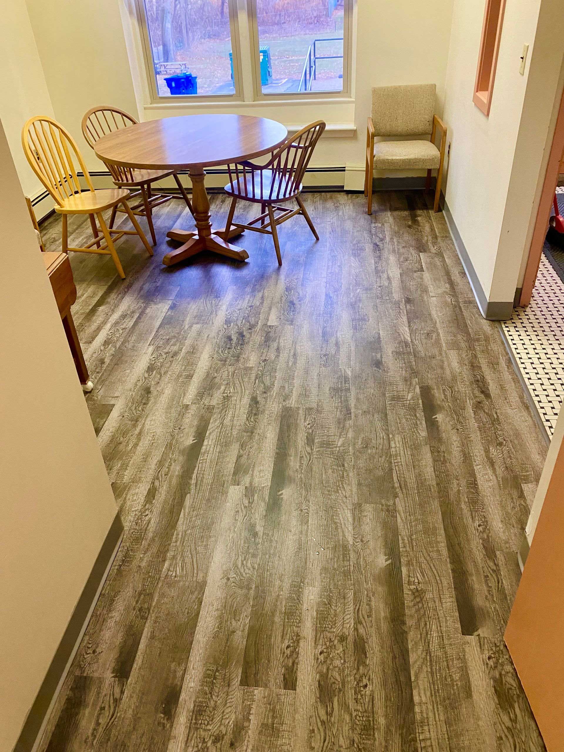 Dining room with wood-look flooring, a round wooden table, and chairs near a window.