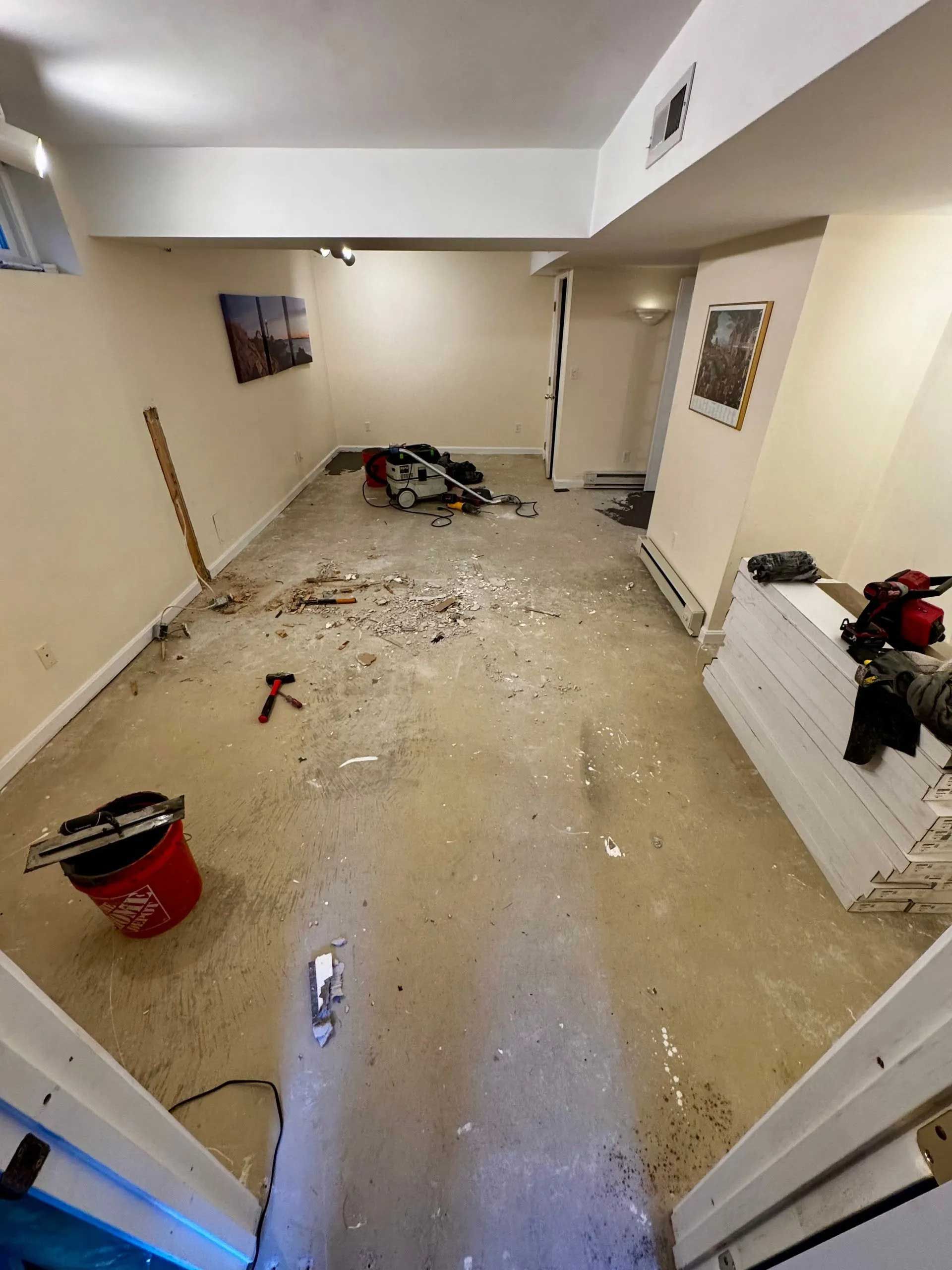 A room under construction with debris on the floor, tools, and stacks of wood panels.