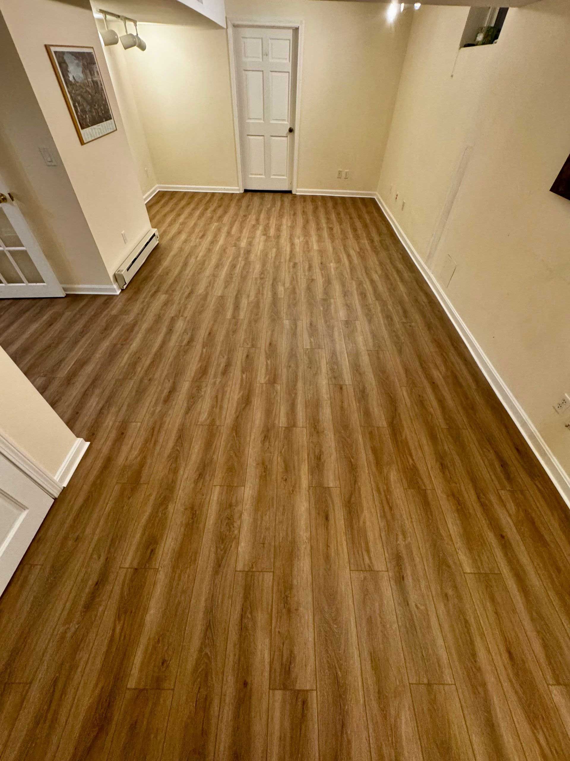 Empty room with wood-look flooring, beige walls, and a closed white door.
