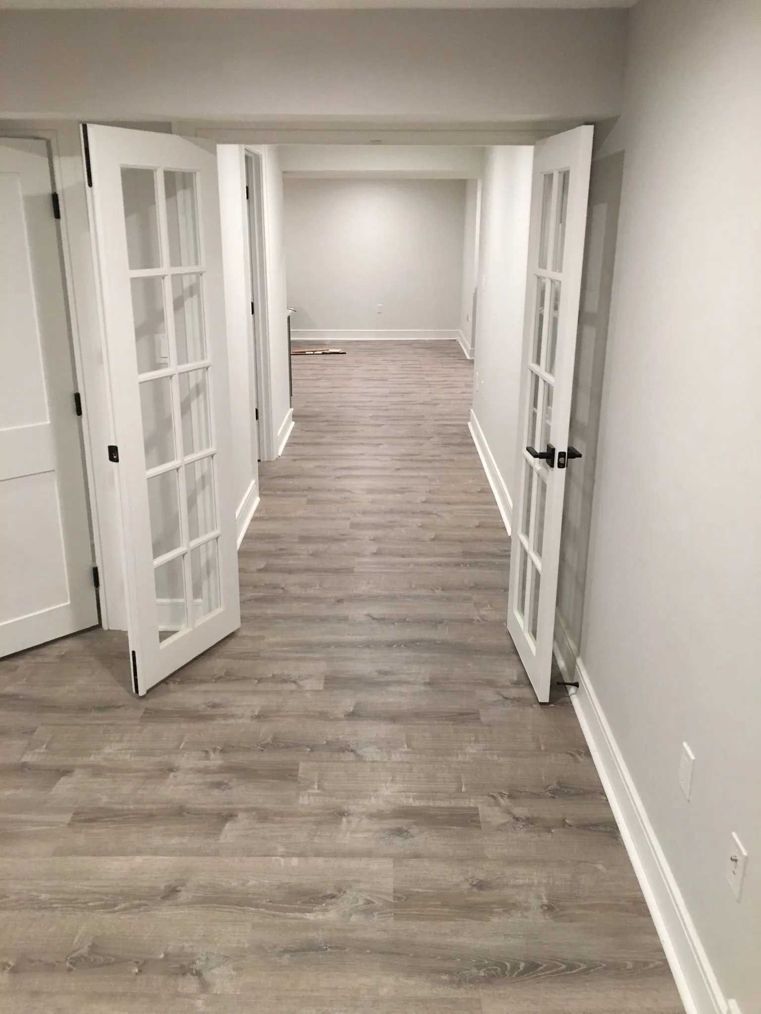 Hallway with white walls, wood-look flooring, and open French doors.