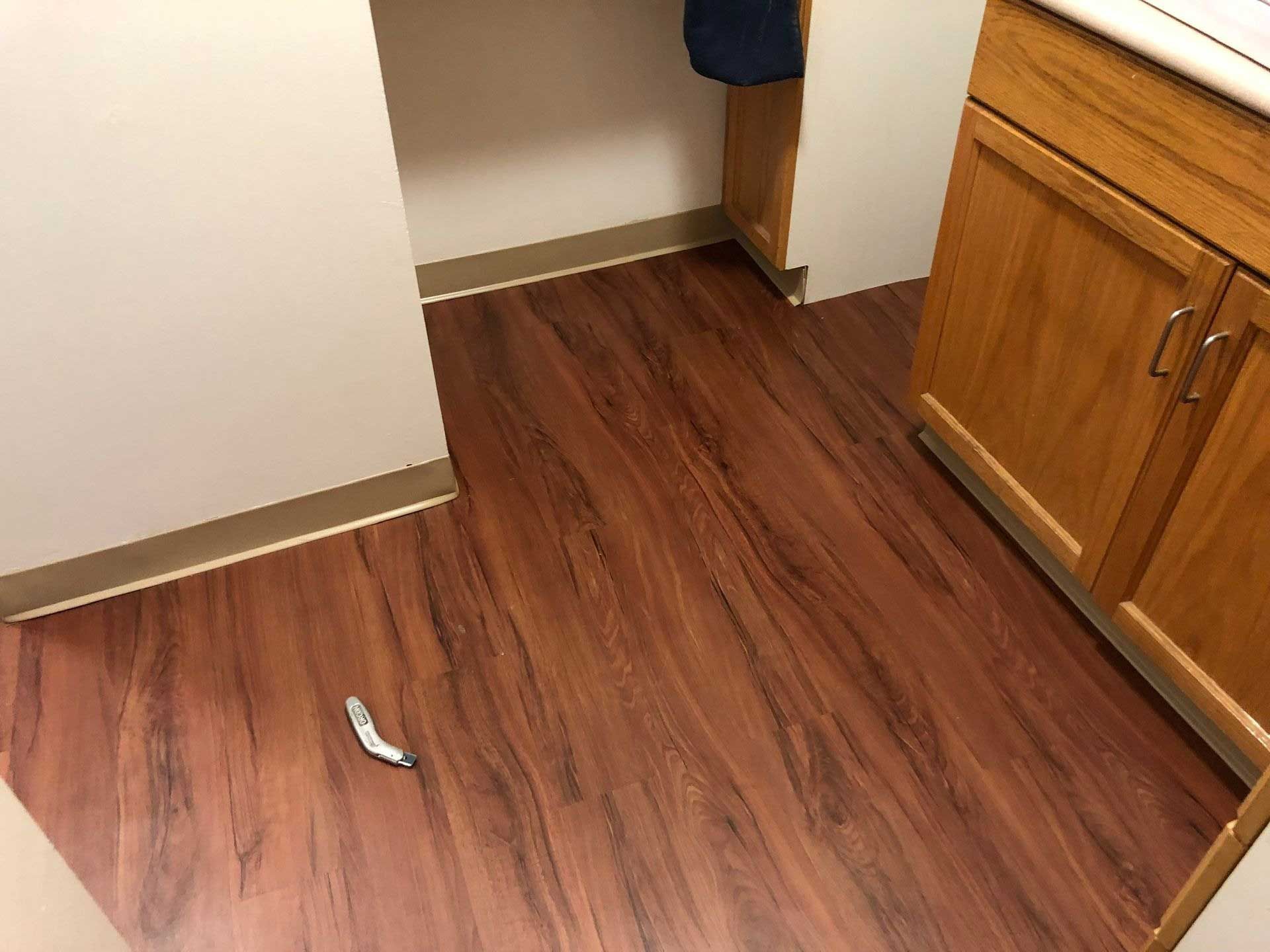 Brown wooden floor with a small object on it, next to a light-colored wall and cabinets.