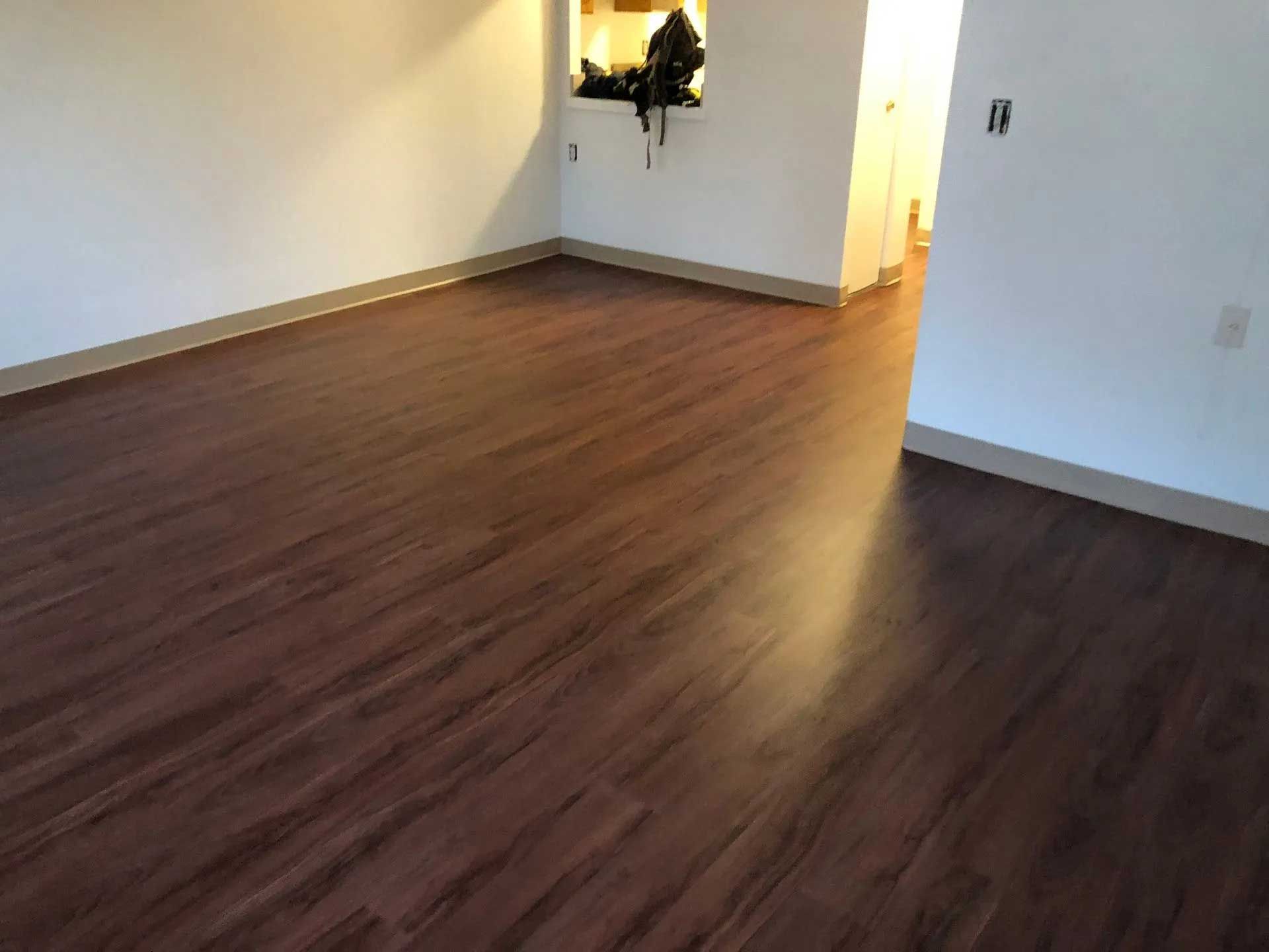 Empty room with dark wood-look flooring, white walls, and a hallway to the right.