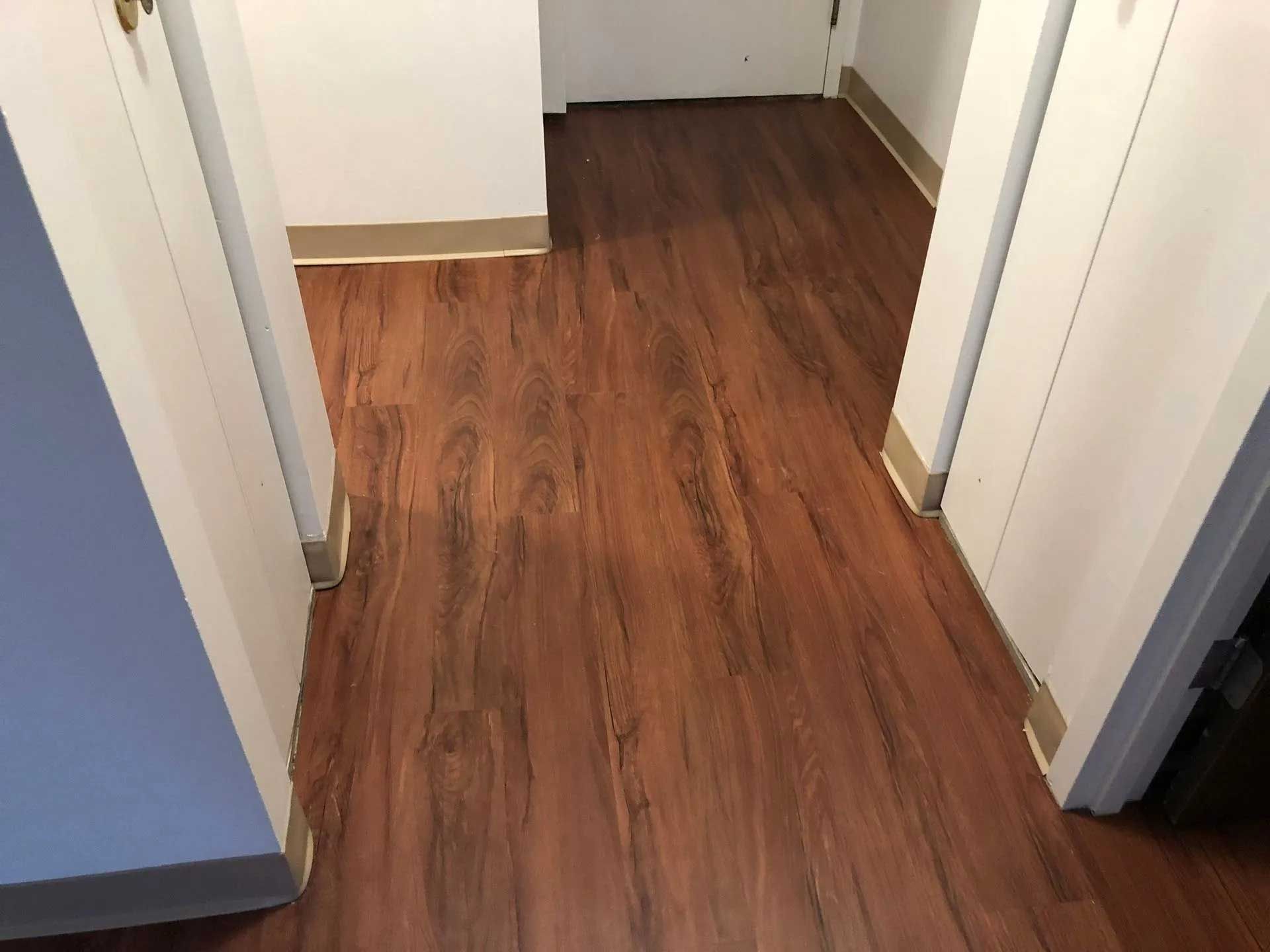 Hallway with wood-look flooring, white doors, and tan baseboards.