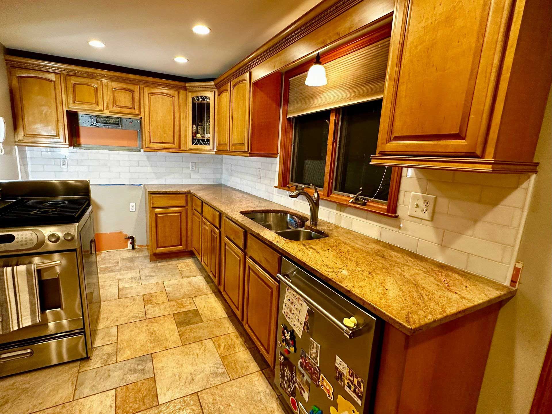 Kitchen renovation with tan cabinets, granite countertops, white subway tile backsplash, and stainless steel appliances.