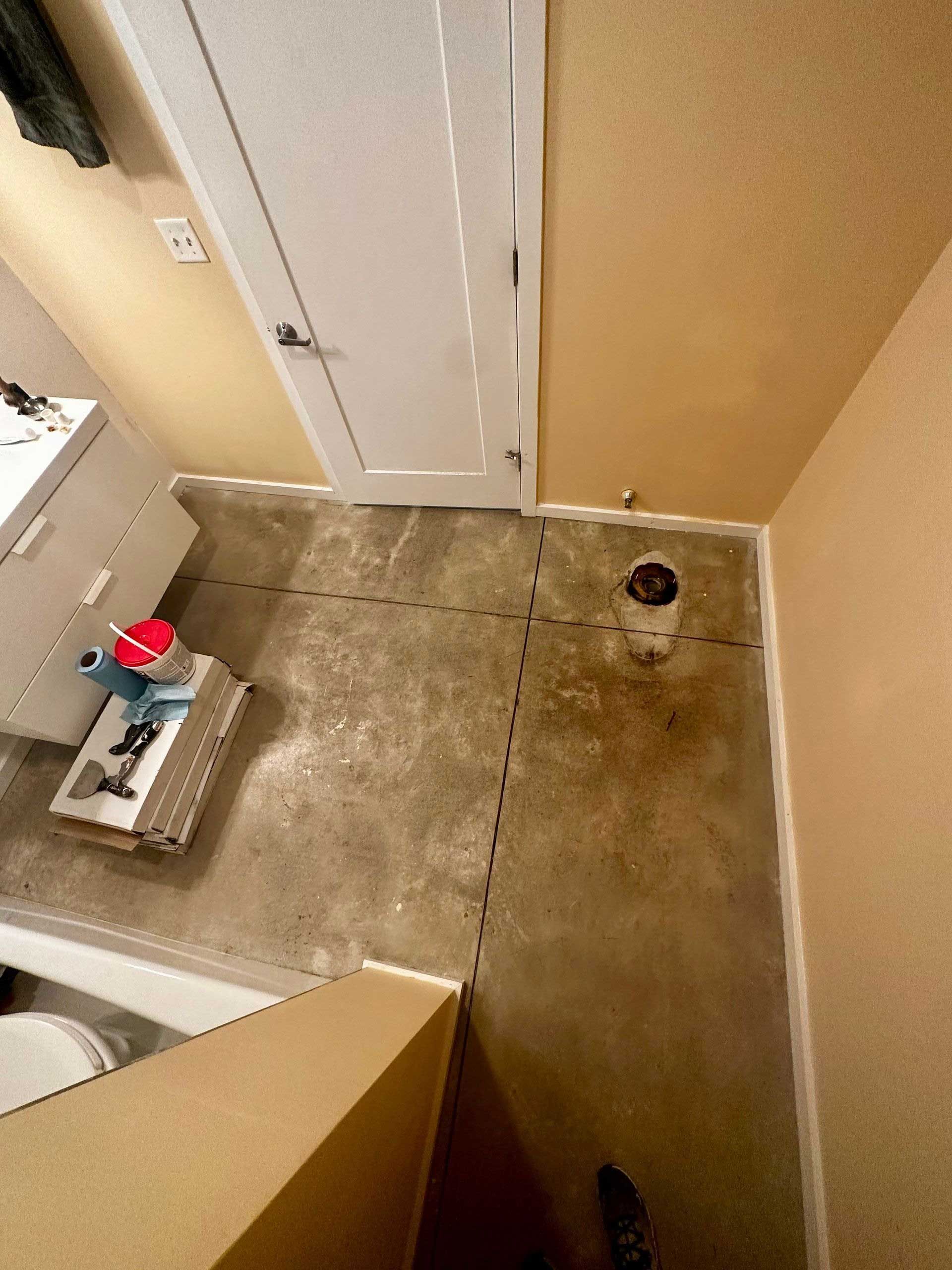 Bathroom with exposed concrete floor, toilet, white door, and beige walls.
