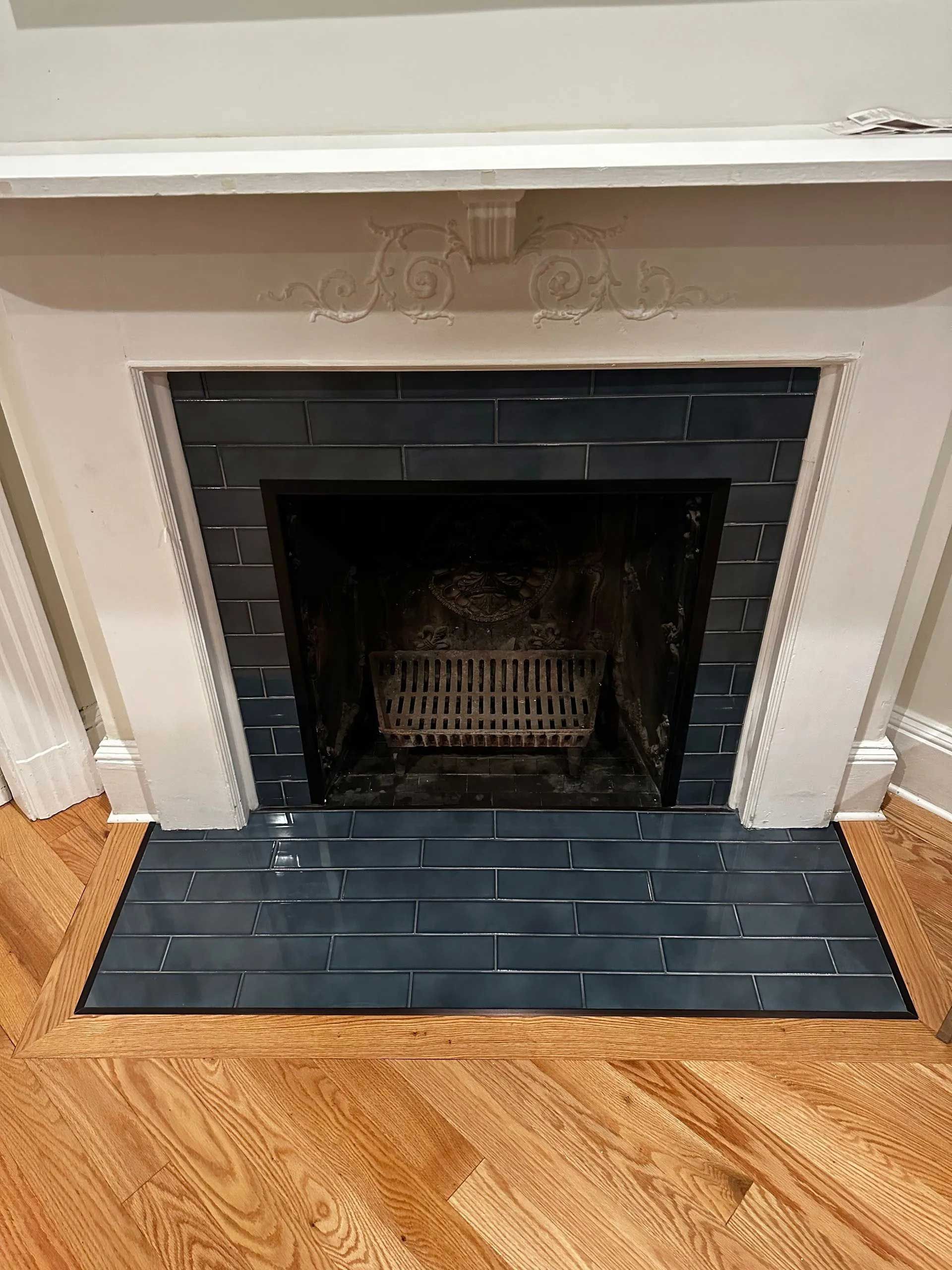 Fireplace with navy-blue tiled surround and hearth, white mantel, and wooden floor.