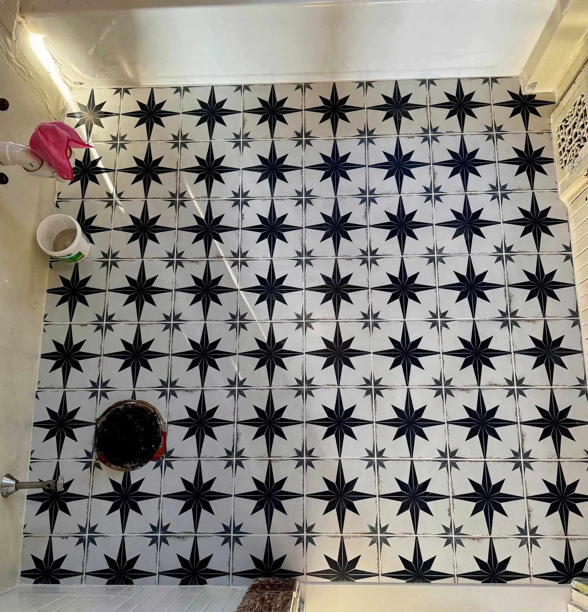 Black starburst-patterned tiles cover a bathroom floor. A pink washcloth and bucket are visible.