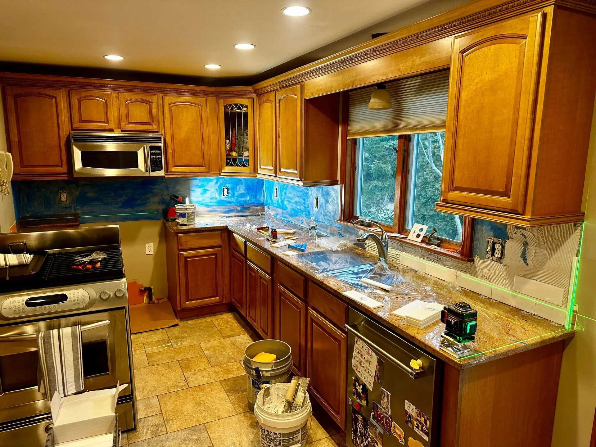 Kitchen with brown cabinets, granite counters, and blue backsplash being renovated.