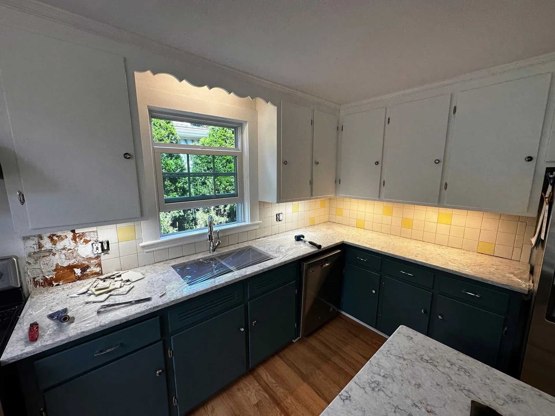 Kitchen with dark teal cabinets, white countertops, white uppers, and a window.