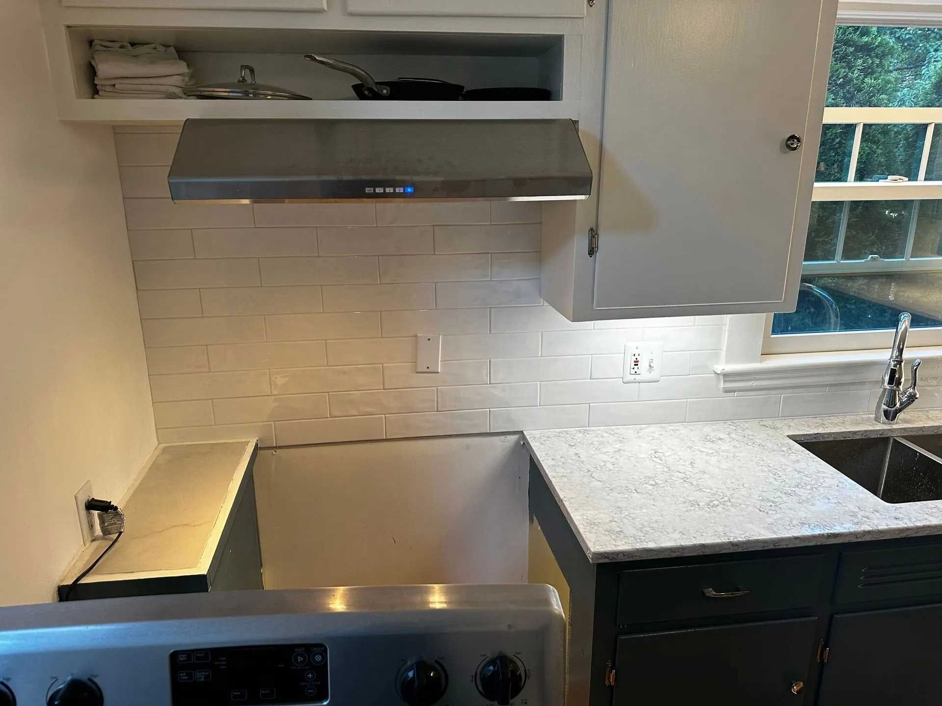 Kitchen with range, white subway tile backsplash, stainless steel hood, and granite countertops.
