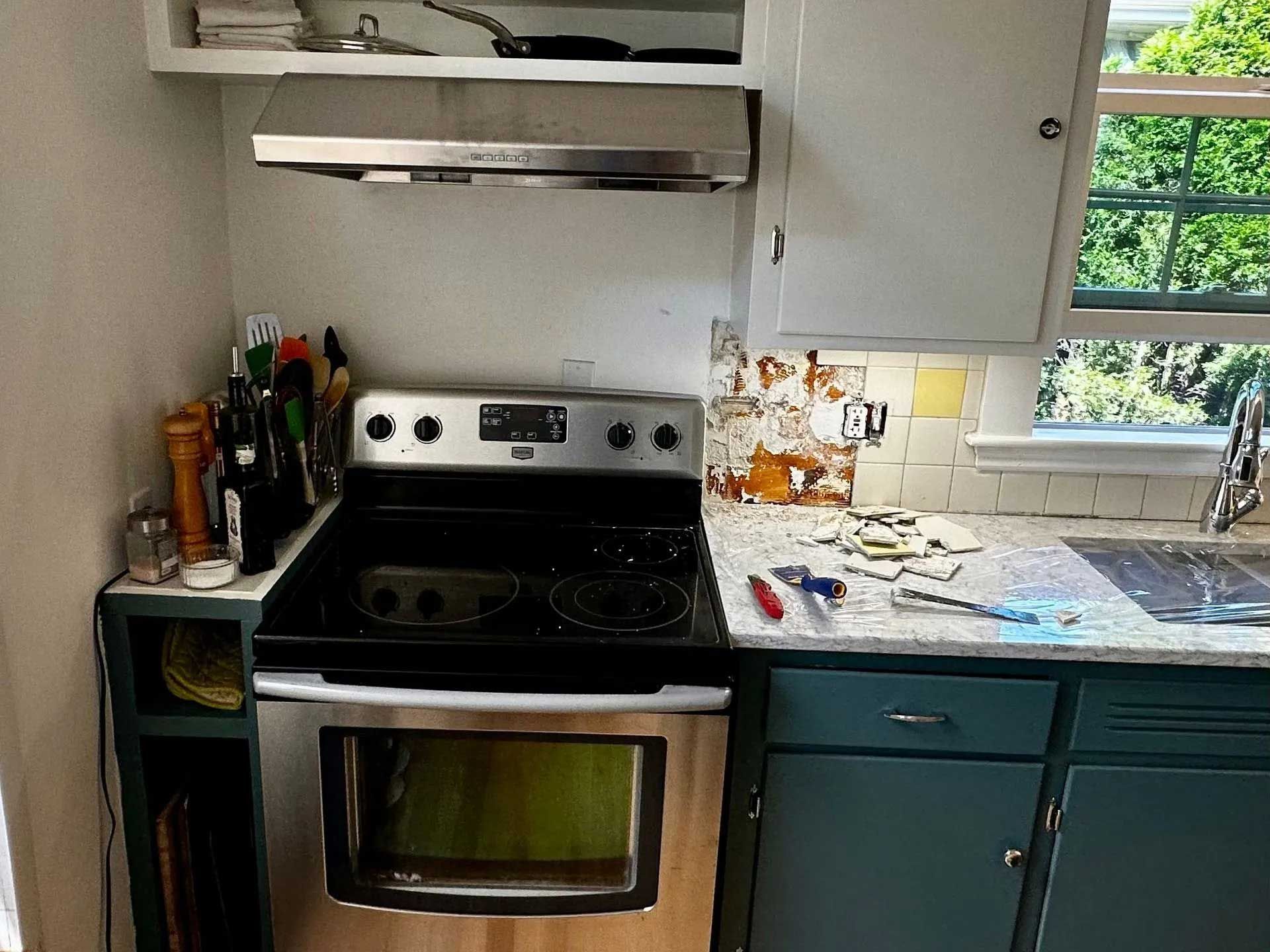 A kitchen with a stainless steel stove, teal cabinets, and a window overlooking greenery.