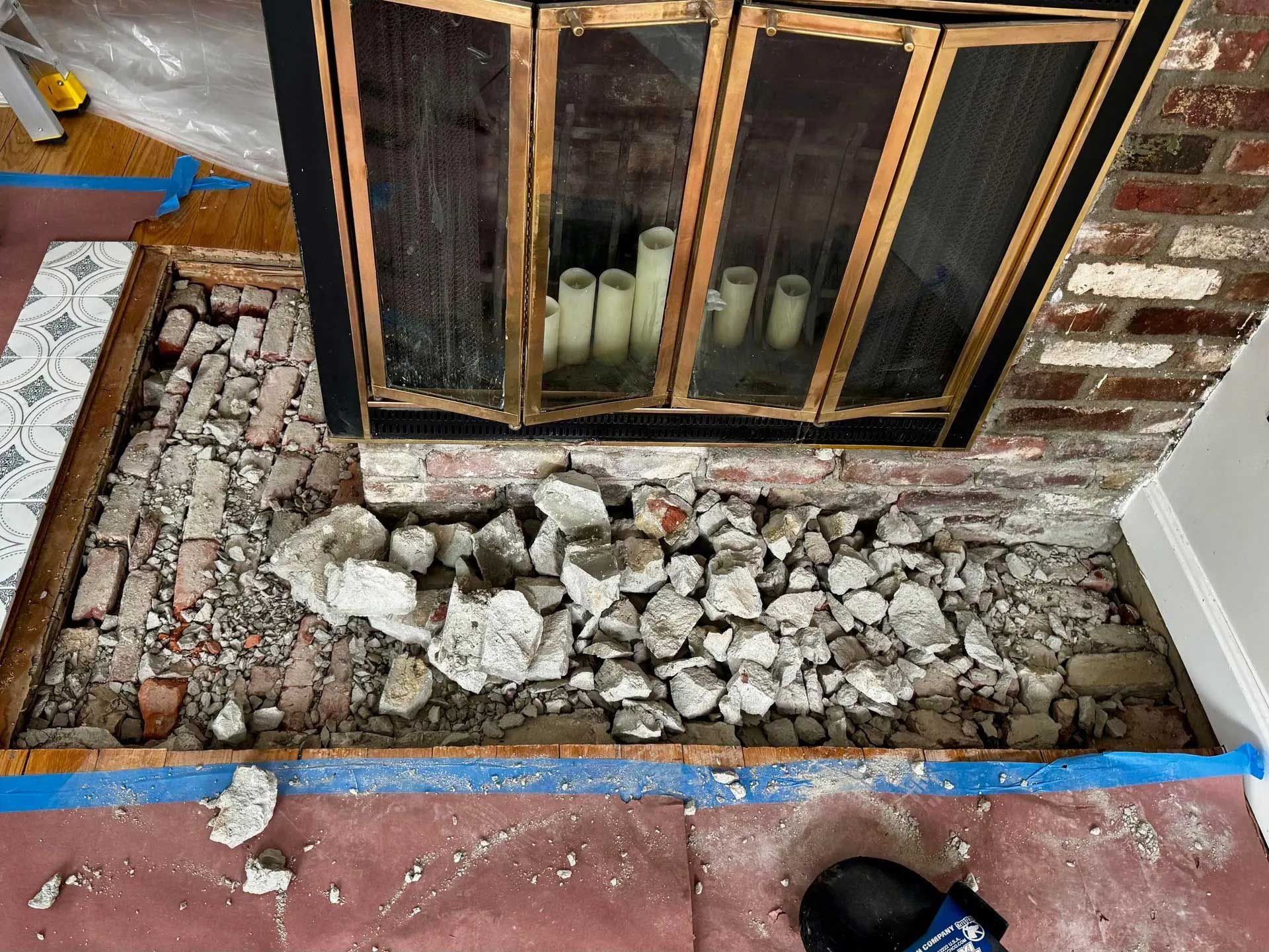 Fireplace hearth demolition: brick and concrete debris, wood frame, blue tape, red flooring, brick wall.