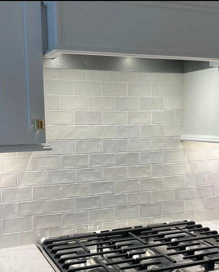 White subway tile backsplash behind a black gas stove, beneath a stainless steel range hood and cabinets.