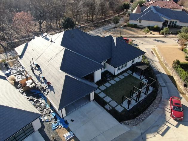 Aerial view of a modern house with a dark gray roof, a carport, and a red car parked on the street.