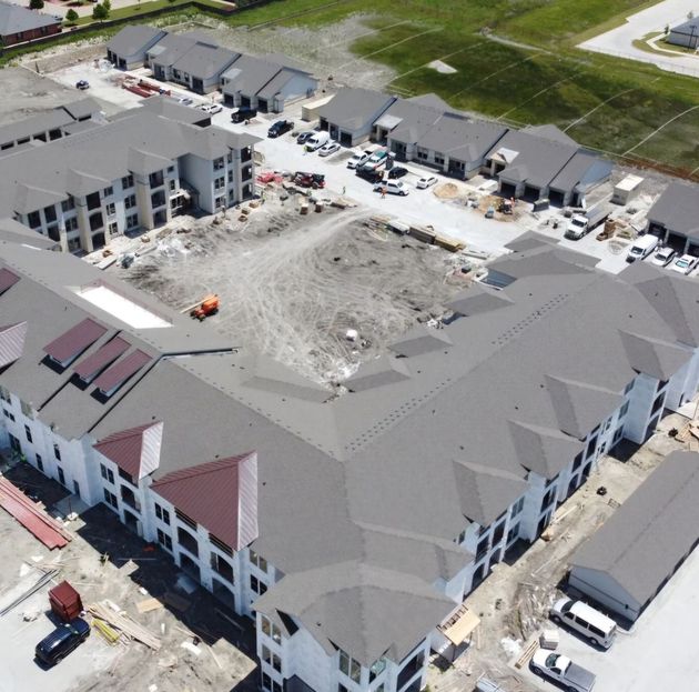 Aerial view of a modern house with a dark gray roof, a carport, and a red car parked on the street.