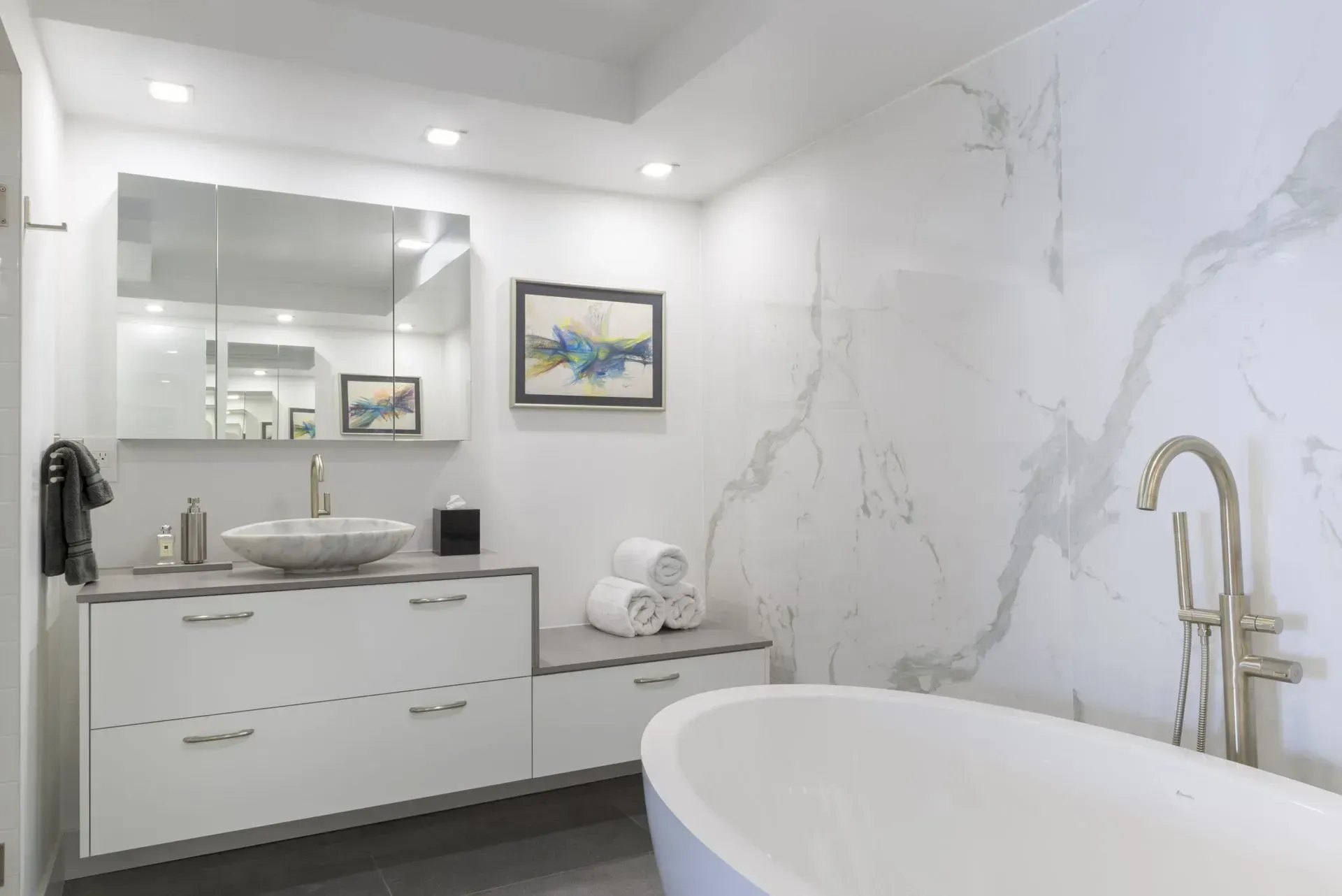Bright white modern bathroom with double vanity, large mirror, and freestanding tub beside marble-look walls.