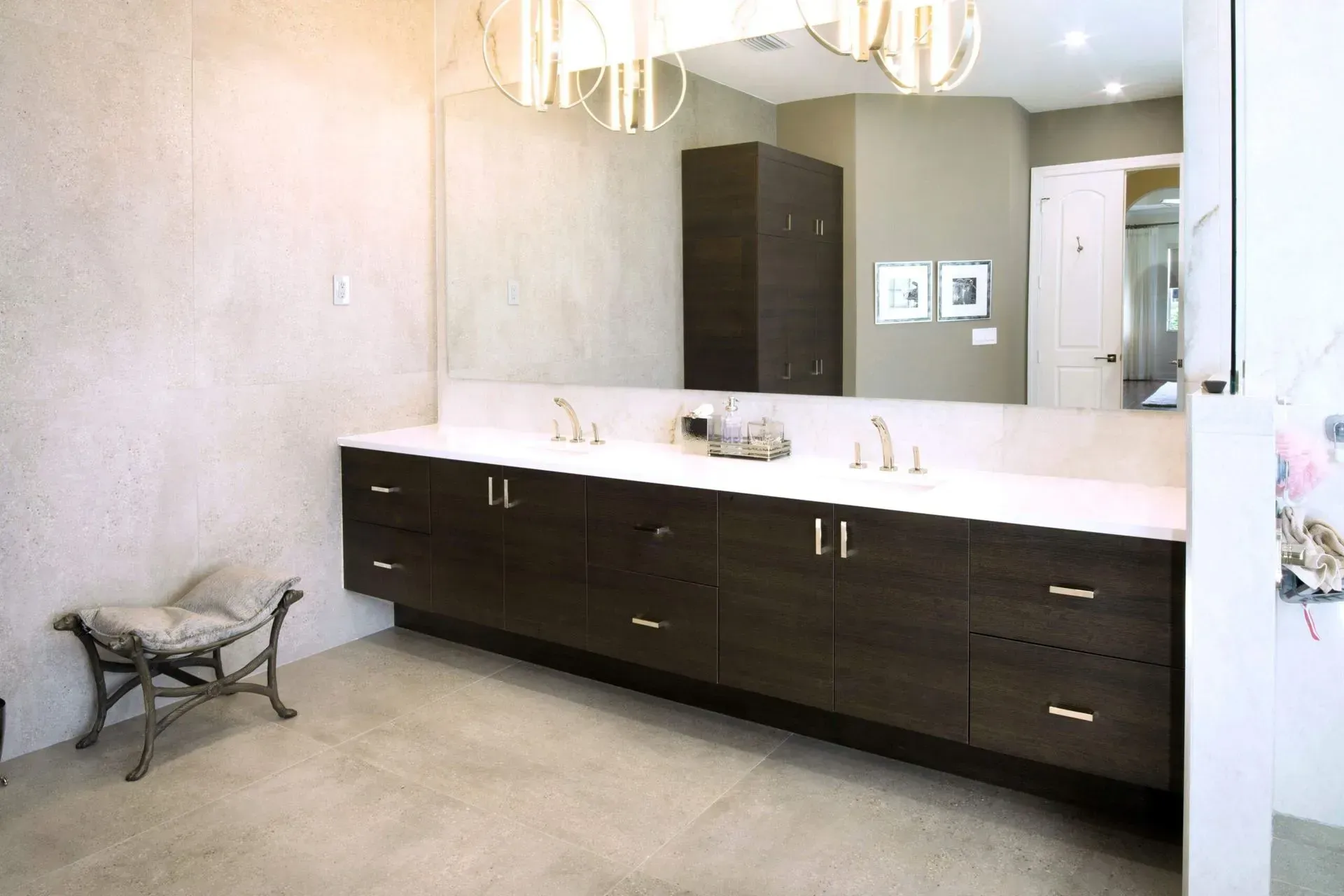Modern bathroom with dark wood vanity, white countertop, large mirror, and chandelier lighting.