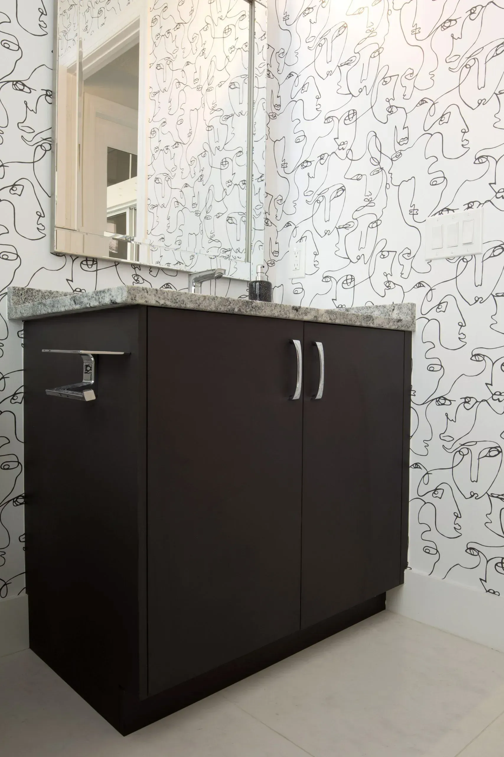 Dark bathroom vanity with sink and mirror against patterned white walls.