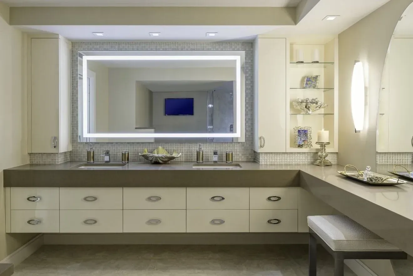Modern bathroom vanity with large illuminated mirror, double sinks, and beige cabinetry.