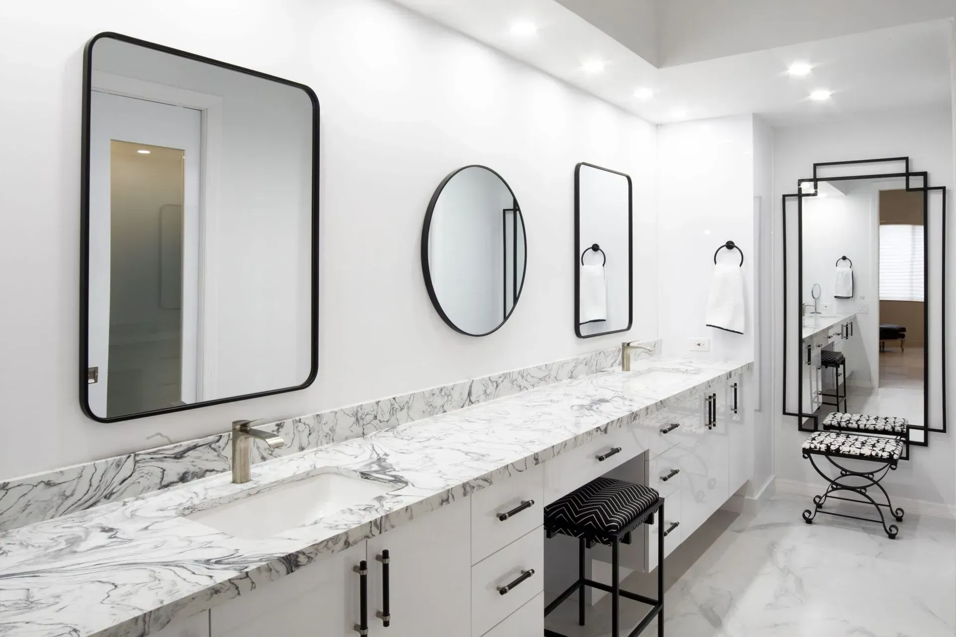 Bright white bathroom vanity with marble counters, large mirrors, and black stools in a modern interior.