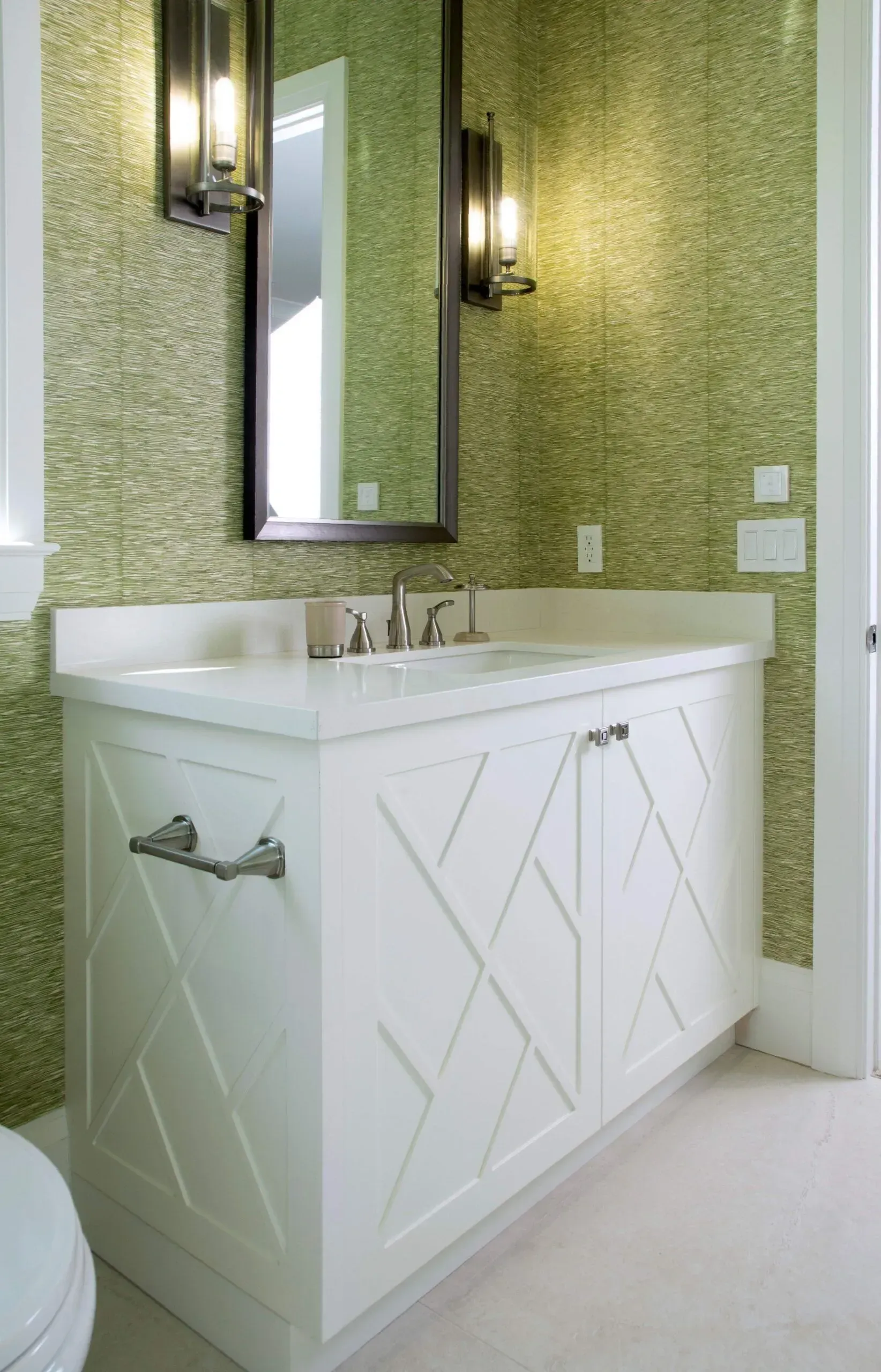 White bathroom vanity with sink and mirror against green mosaic tile walls.