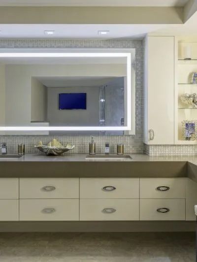 Modern bathroom vanity with large backlit mirror, double sinks, and beige cabinetry.