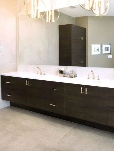Modern bathroom vanity with dark wood cabinets, white countertop, and large mirror under pendant lights.